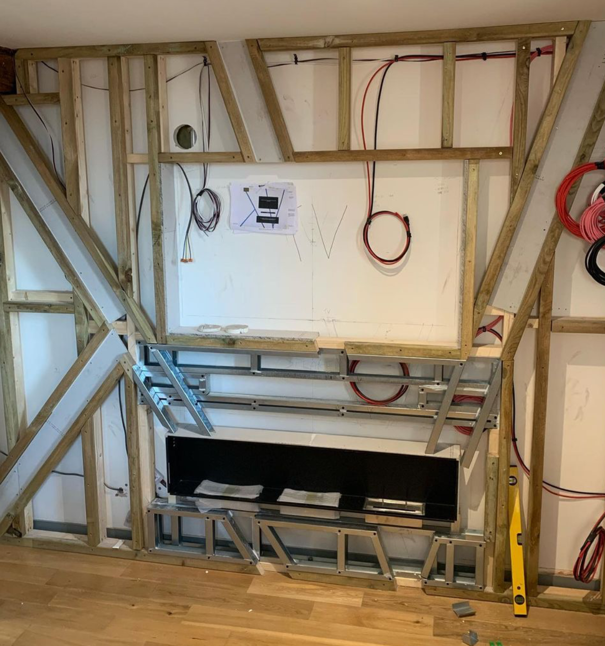 Interior view of a room under construction with exposed wooden framing, electrical wiring, and metal framework for wall installation.