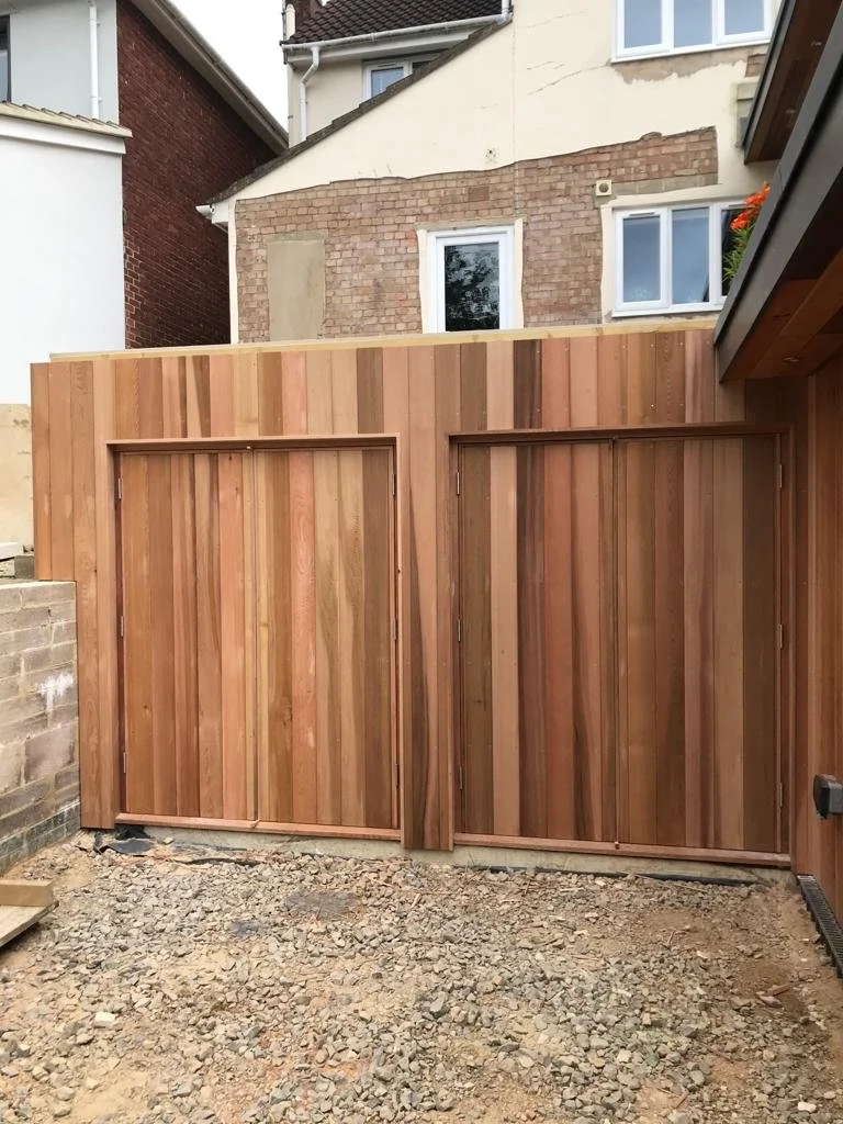 New wooden fence installed in a backyard with dirt ground, adjacent to a brick wall and white house exterior.