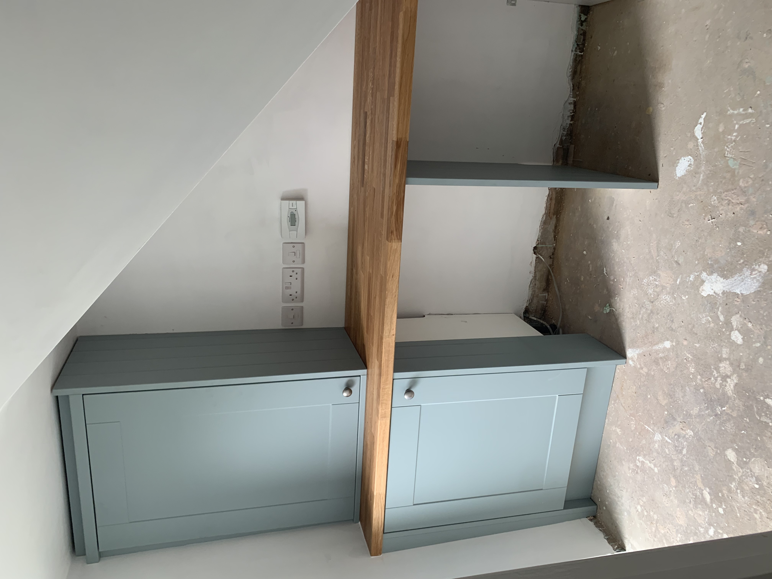 Empty unfinished room with light blue cabinetry, a wooden countertop, and visible electrical outlets and wiring.