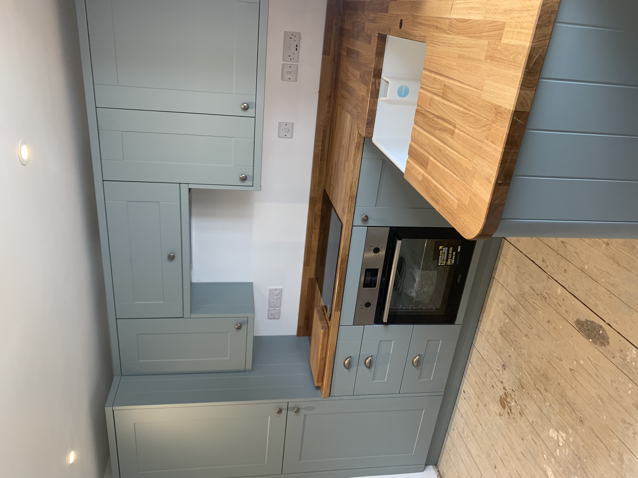 Kitchen with light blue cabinets, wooden countertops, a built-in oven, and a wooden wall on the floor.