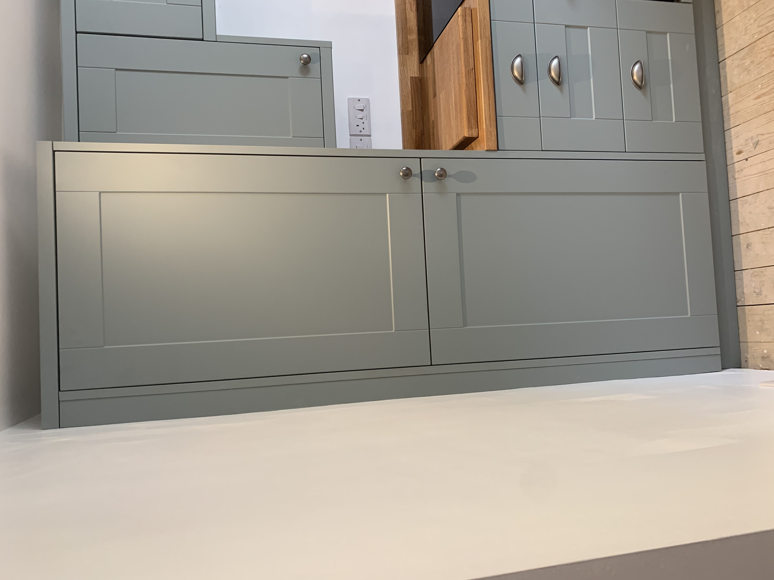 Gray kitchen cabinet with a wooden cutting board on the countertop and a white wall with electrical outlets behind it.