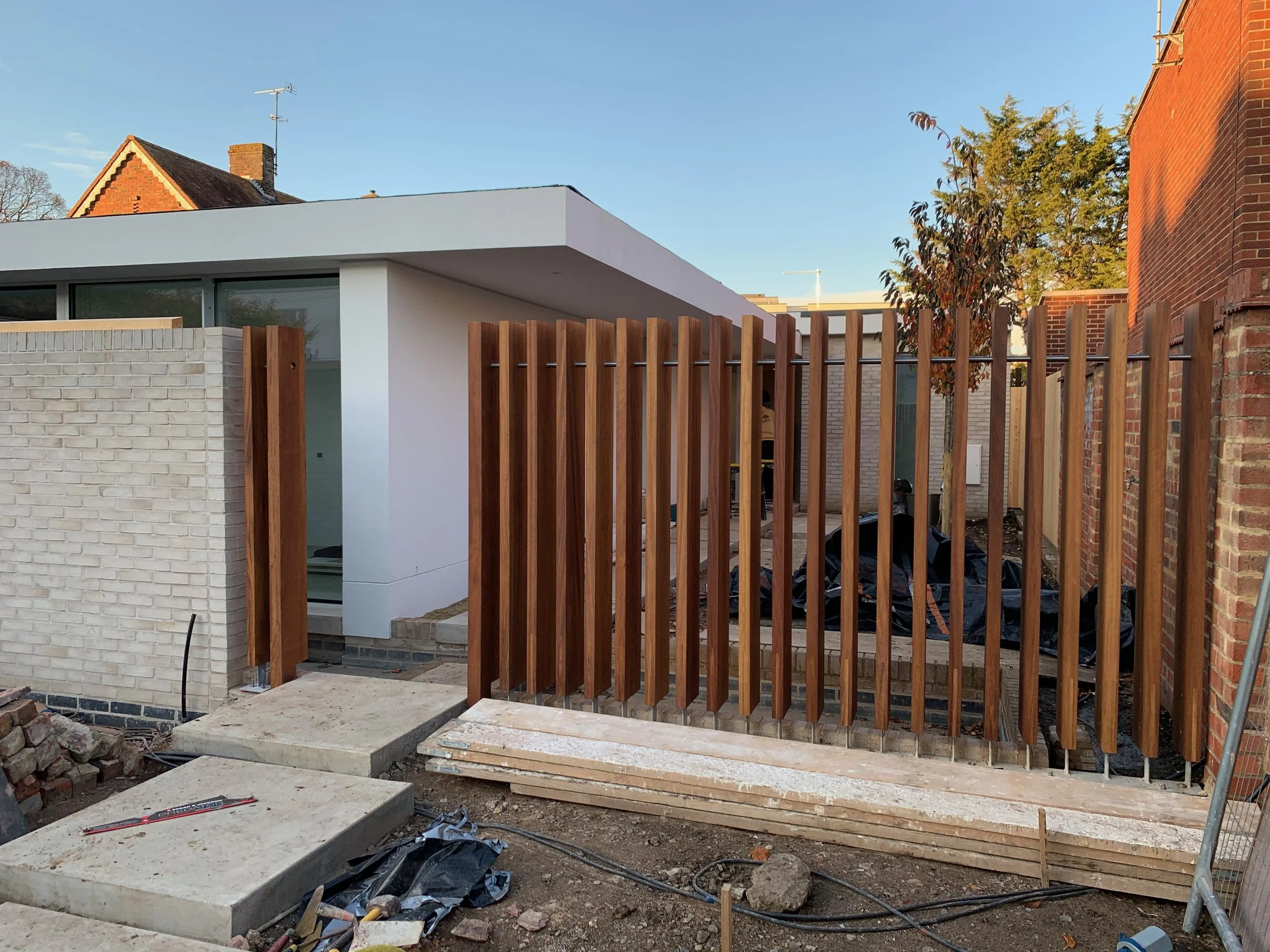 View of a modern backyard construction site with a white building, wooden fence, and concrete steps.