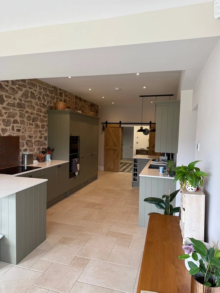 Modern kitchen with green cabinets, stone accent wall, tiled floor, wooden sliding barn doors, and potted plants.