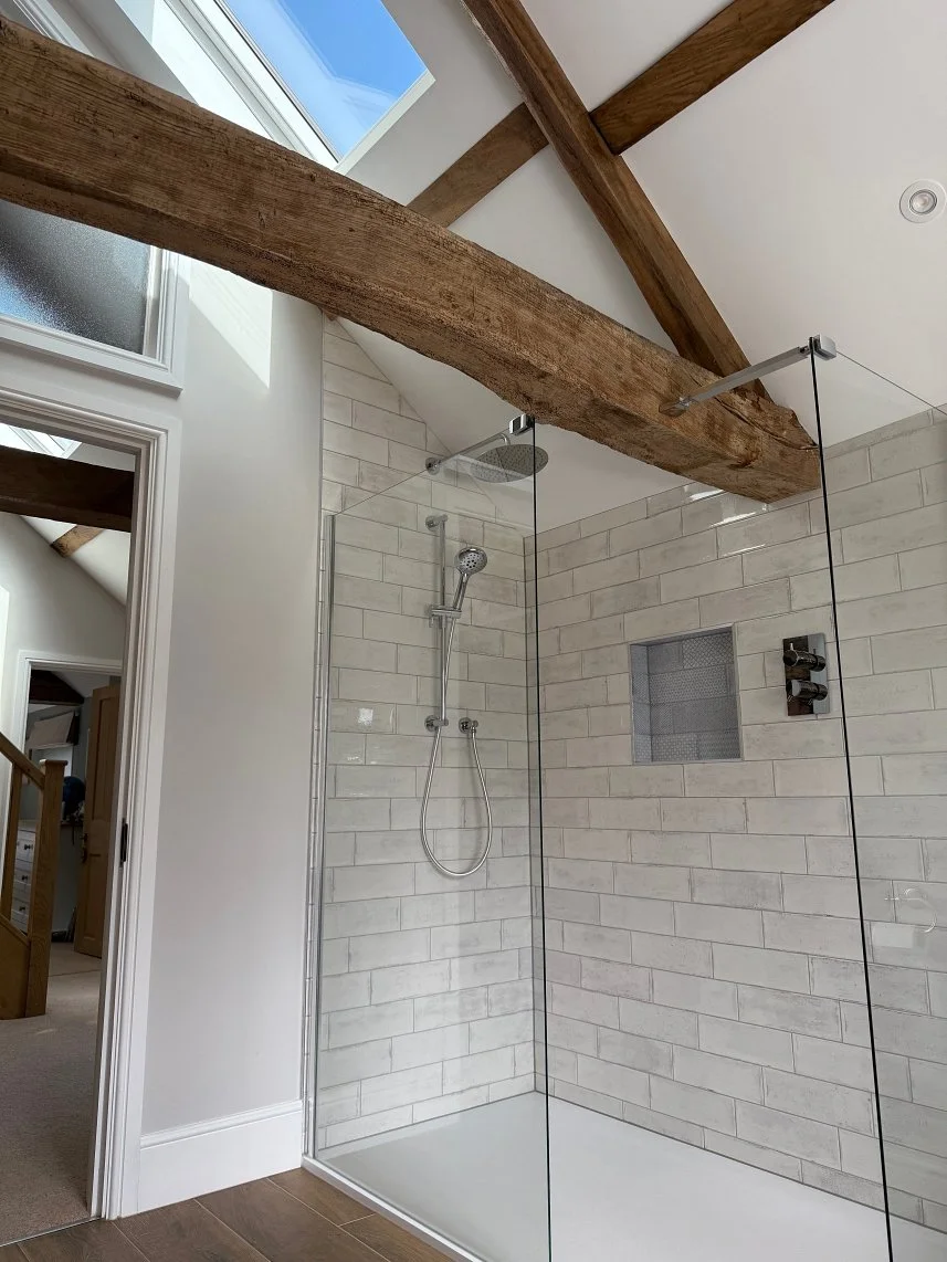 Modern walk-in shower with white subway tiles, a rain showerhead, a handheld shower, a niche for storage, and exposed wooden beams on the ceiling.