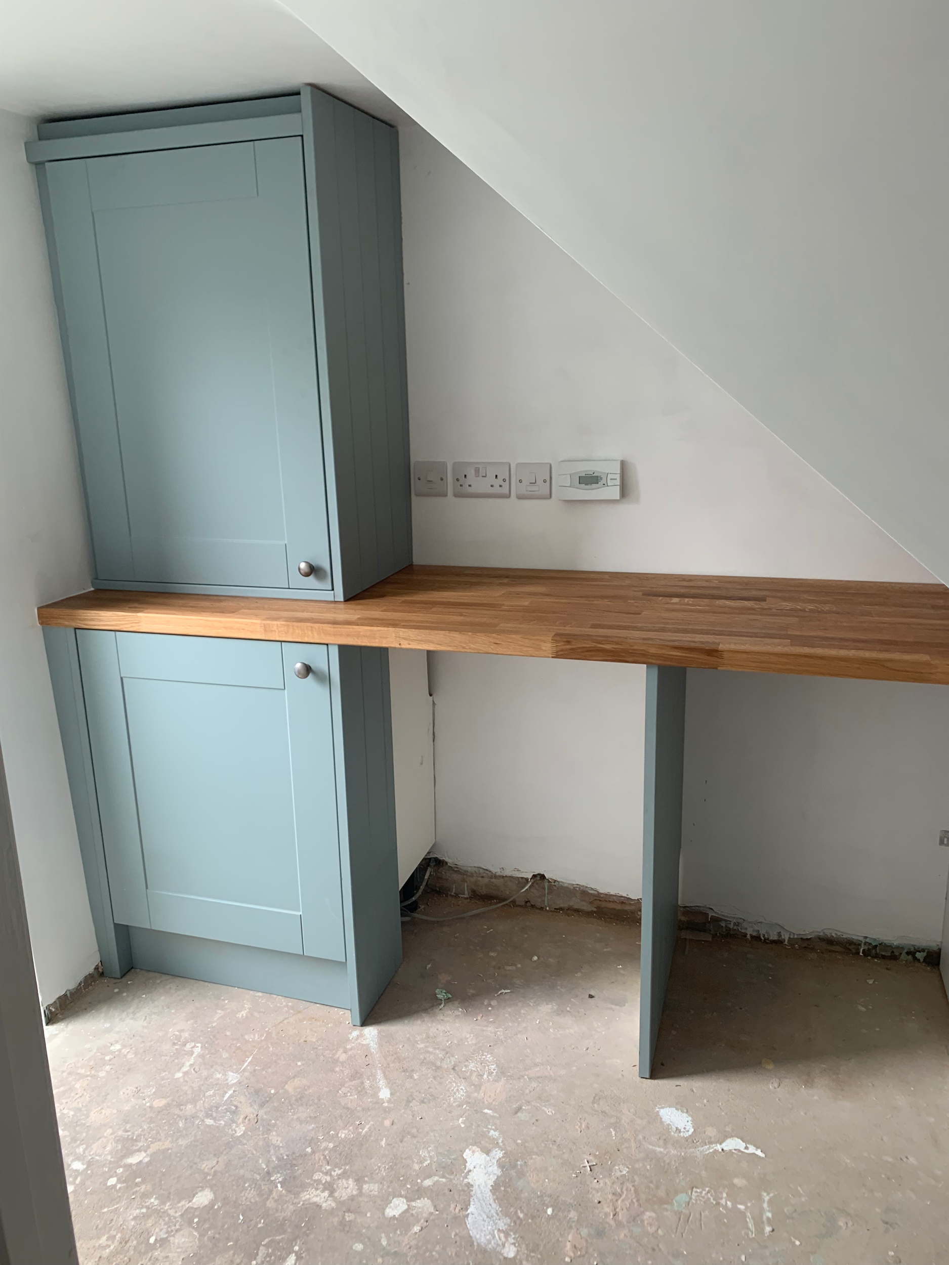 Empty unfinished room with light blue cabinetry, a wooden countertop, and visible electrical outlets and wiring.