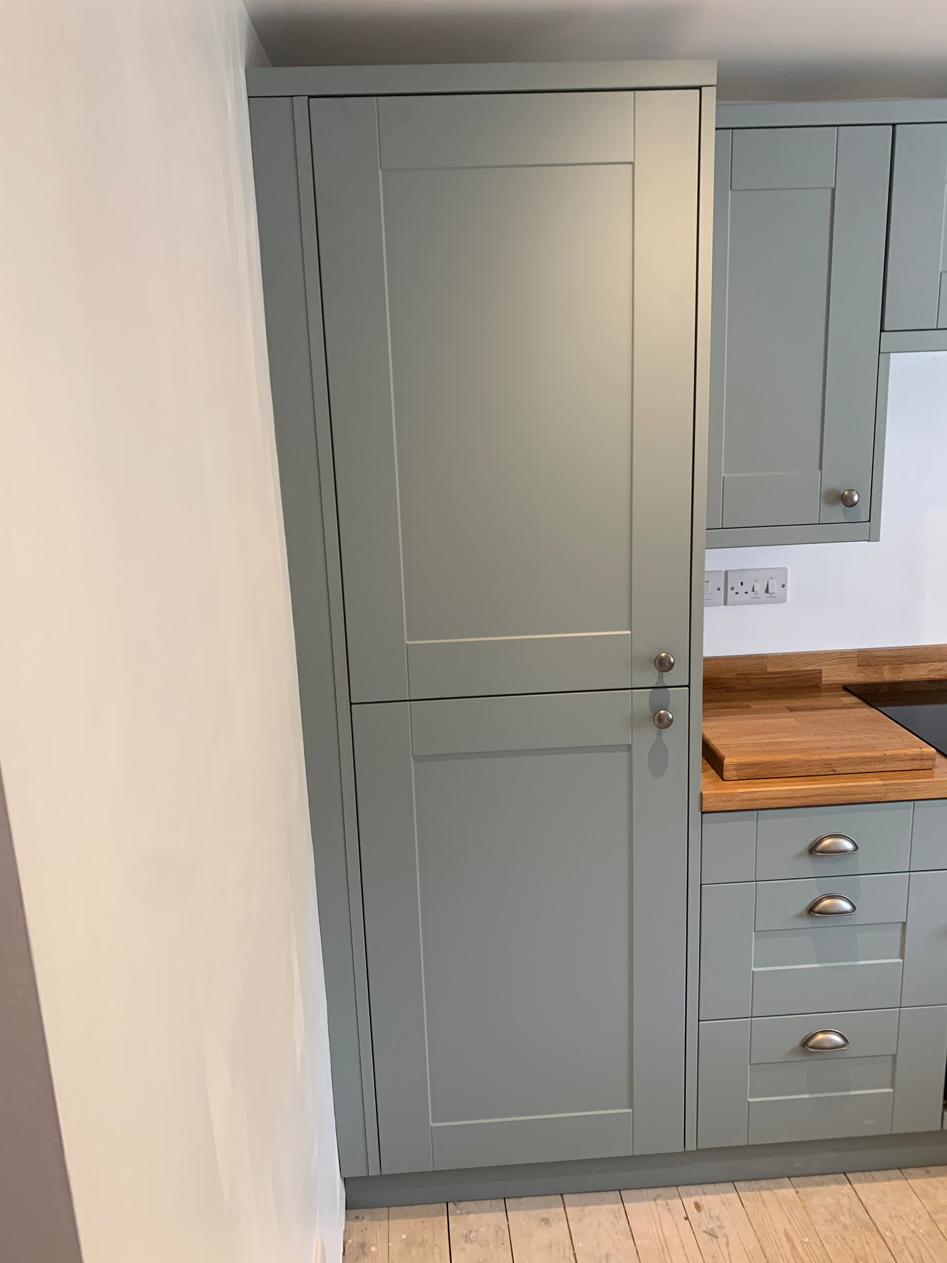 Gray kitchen cabinet with a wooden cutting board on the countertop and a white wall with electrical outlets behind it.