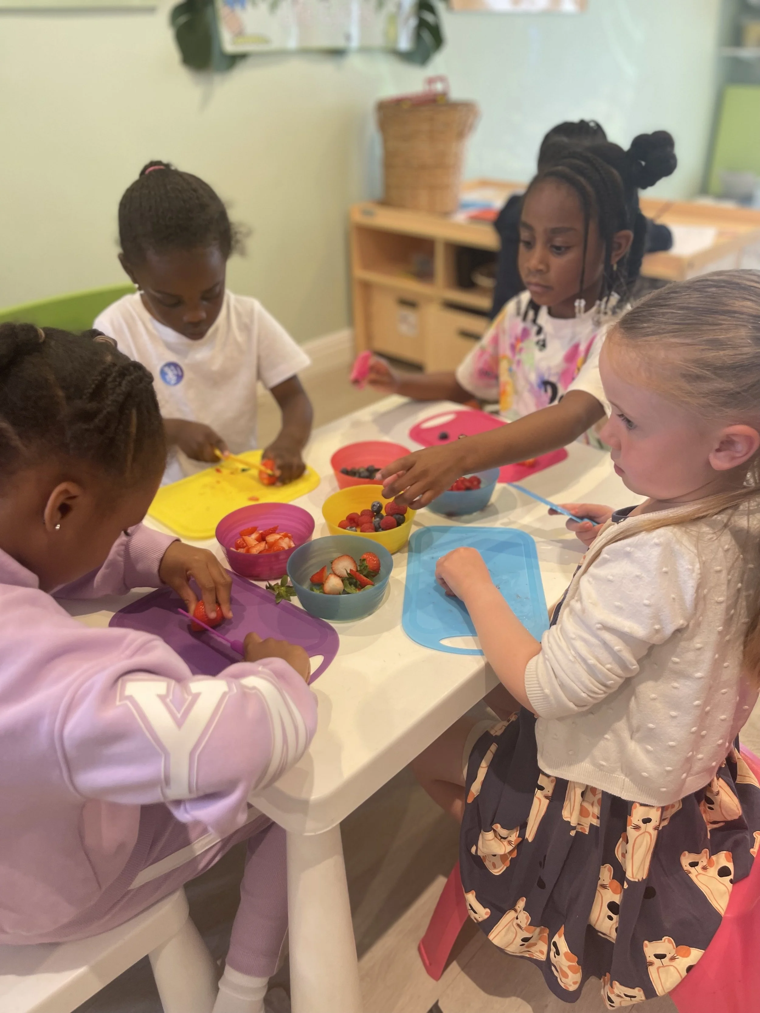 Group of young children at a table preparing and sorting fresh strawberries, blueberries, and raspberries in colorful bowls.