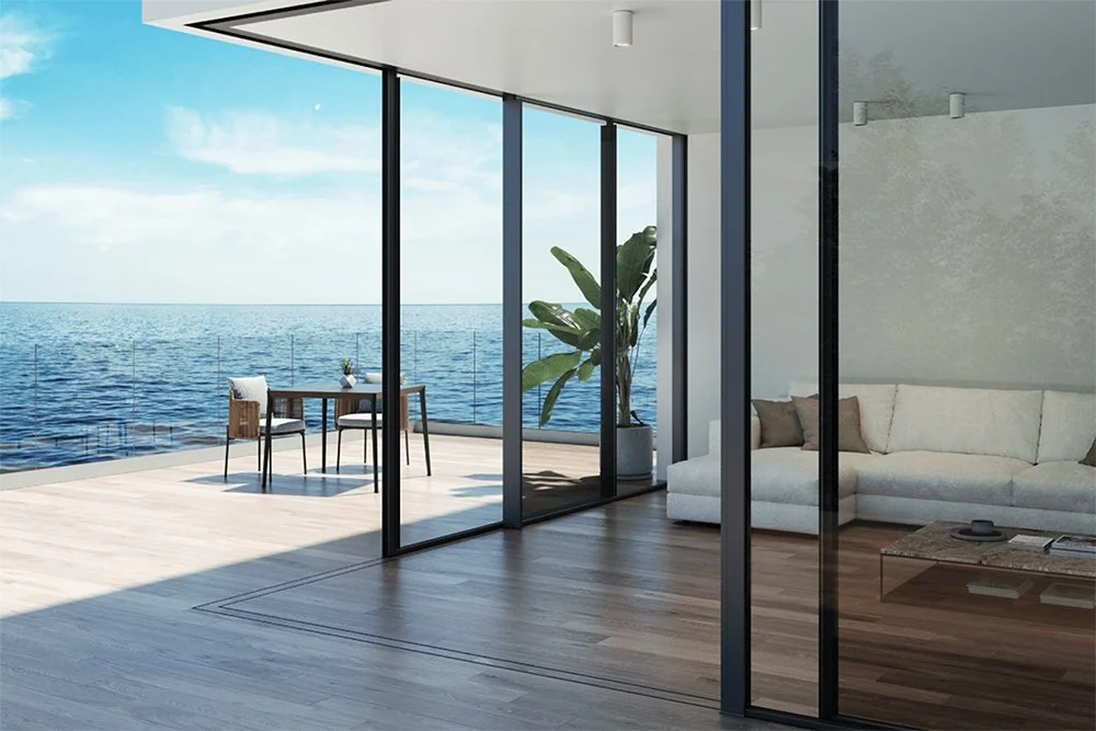 Sala moderna con grandes ventanales con vista al mar, con sillón blanco, mesa de centro y plantas.