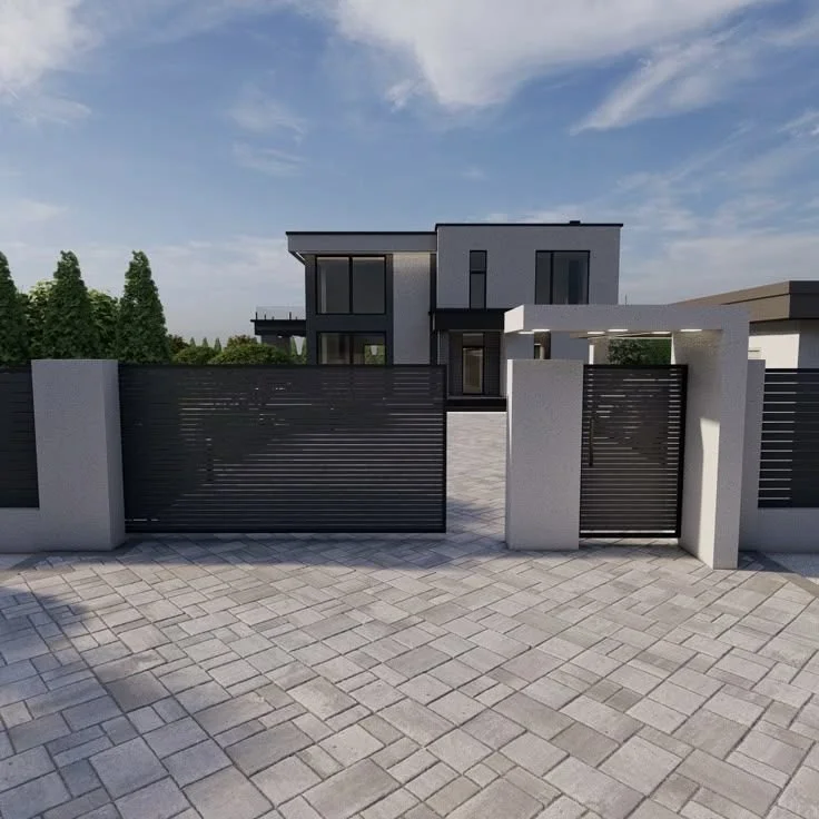 Casa moderna con muro y portón de metal negro, entrada pavimentada, y árboles verdes al fondo