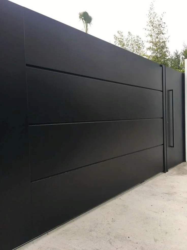 Una puerta elegante de color negro, probablemente de metal, instalada en un muro, con un diseño moderno y minimalista.