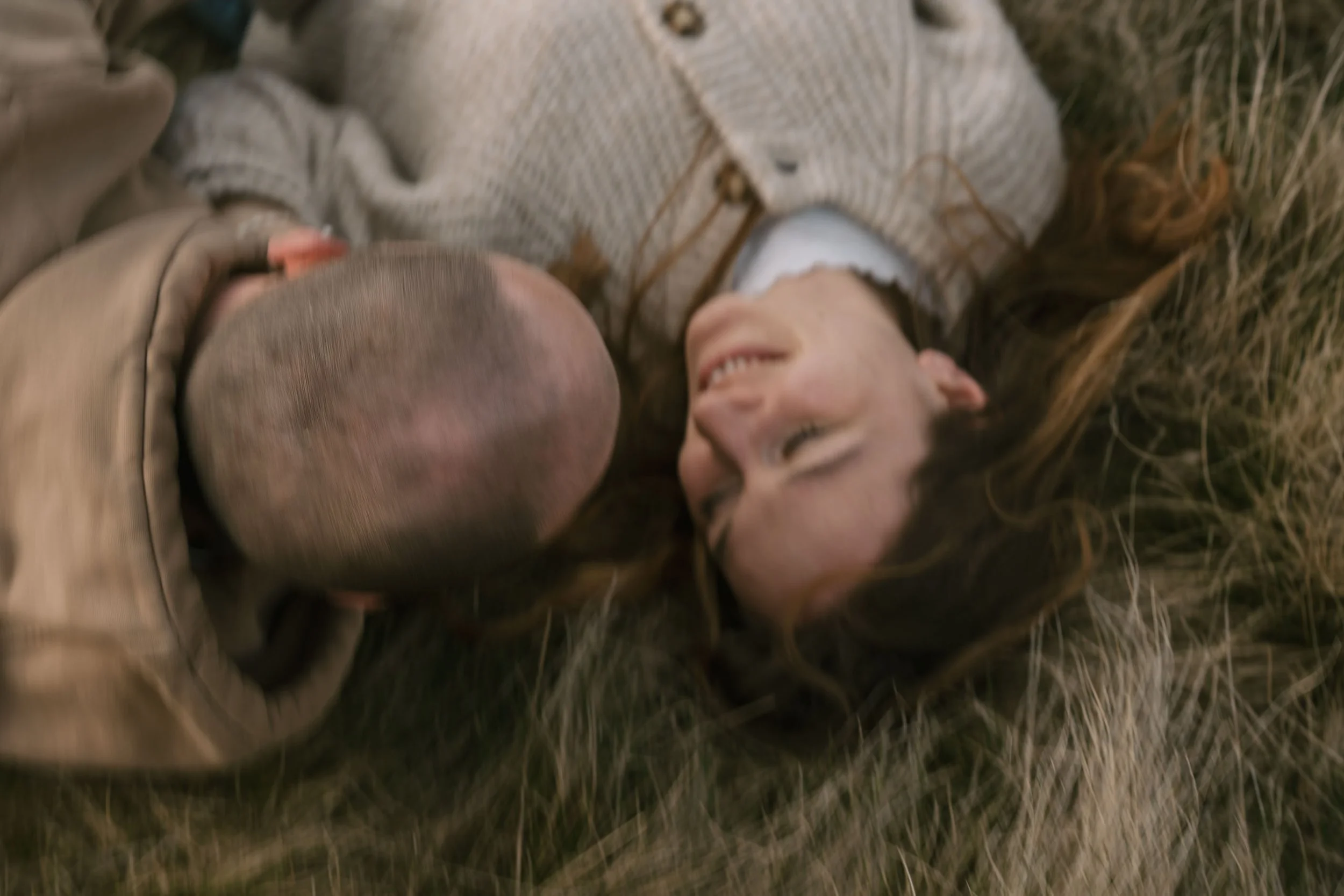 A woman and a child lying on the grass, facing each other, smiling and sharing a joyful moment.