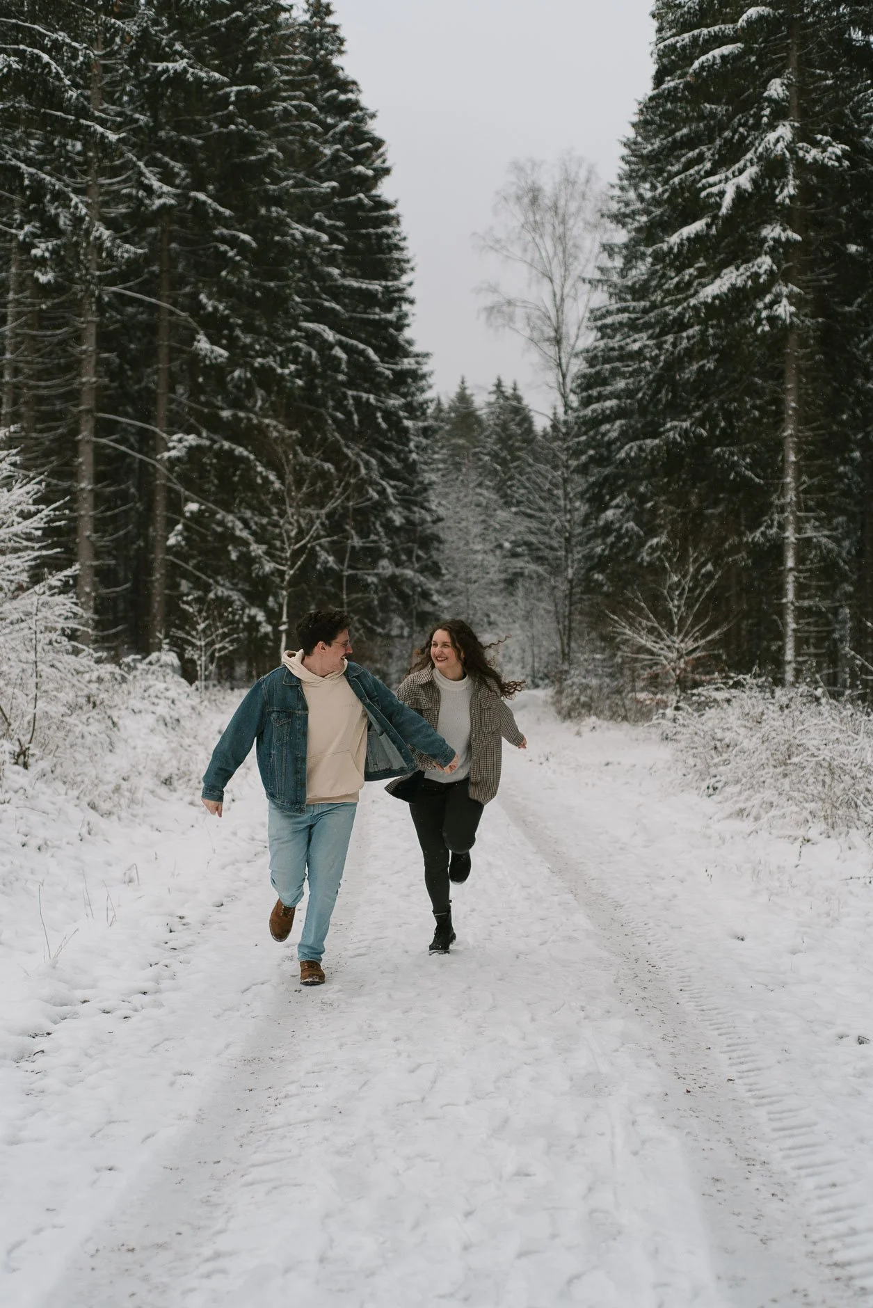 Two people running and playing in the snow on a forest trail during winter.