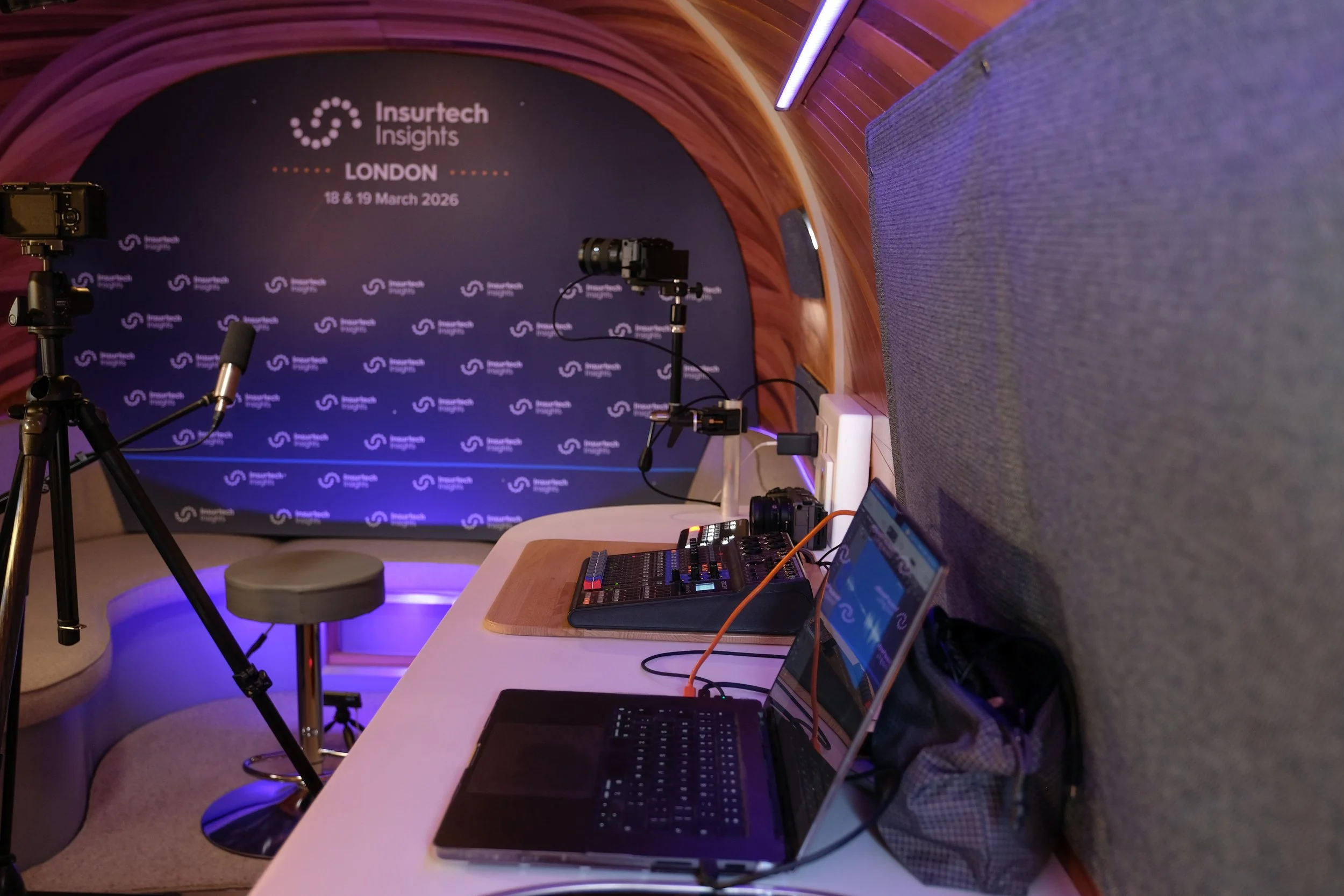 A behind-the-scenes setup at Insurtech Insights conference in London, March 18-19, 2026, featuring cameras, microphones, a mixing console, a laptop, and a seating area with a backdrop displaying the event details.