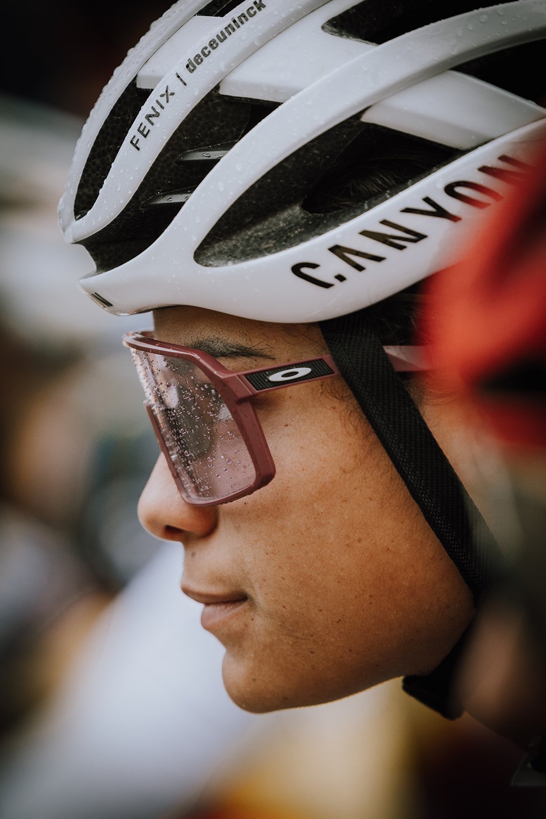 Close-up of a person wearing a white bicycle helmet with black accents and pink tinted glasses with droplets of water on the lenses.