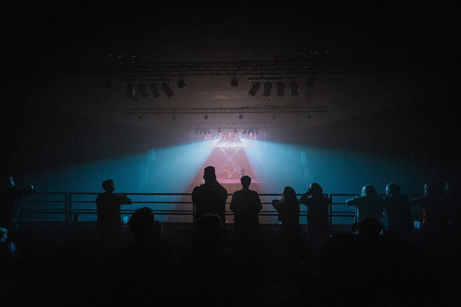 Audience members watching a concert or performance on stage with colorful lighting in a darkened venue.