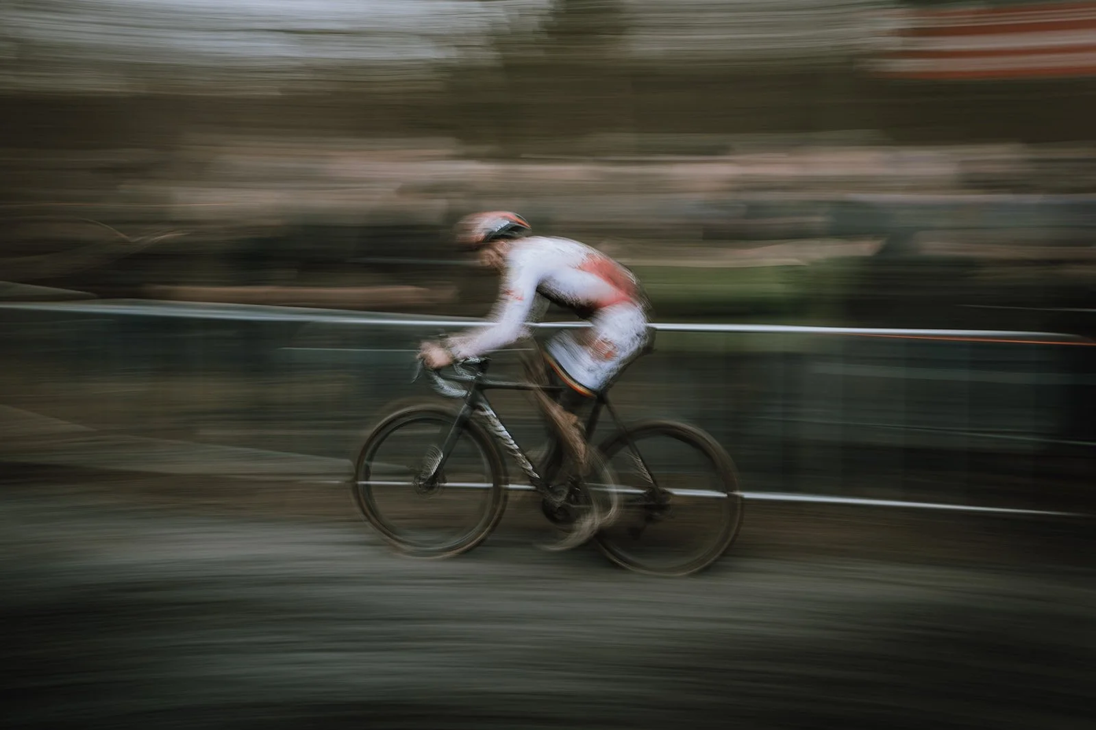 A person riding a bicycle on a trail with motion blur, wearing a helmet and a white and red cycling outfit.