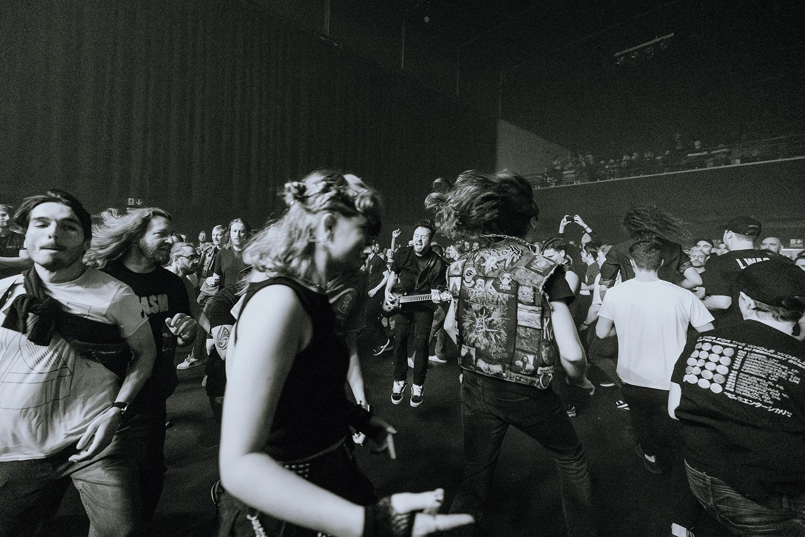 People dancing and enjoying live music at a concert or music event with a musician playing guitar on stage, all in black and white.