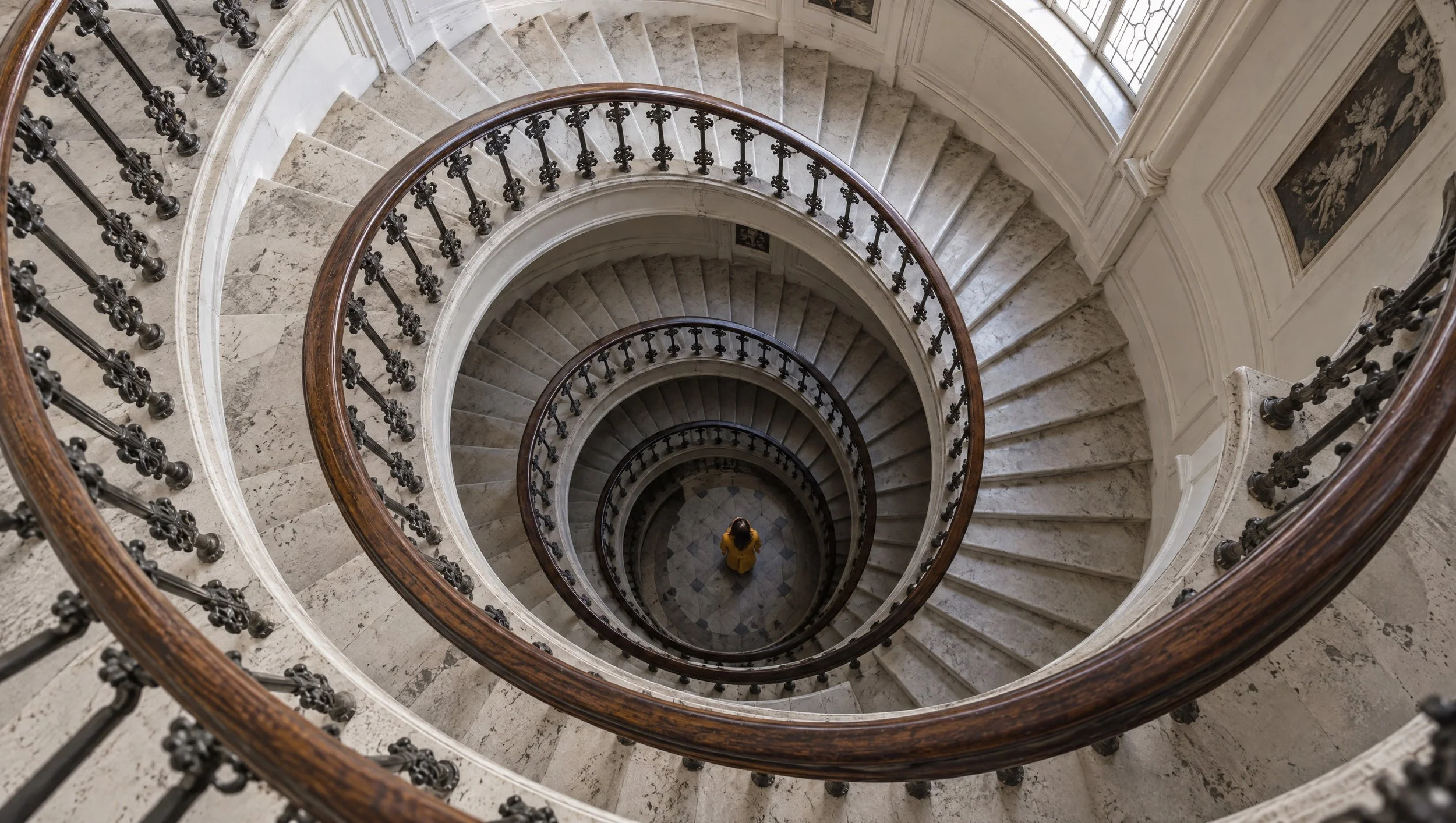 Looking down a spiral staircase at a figure standing at the bottom.