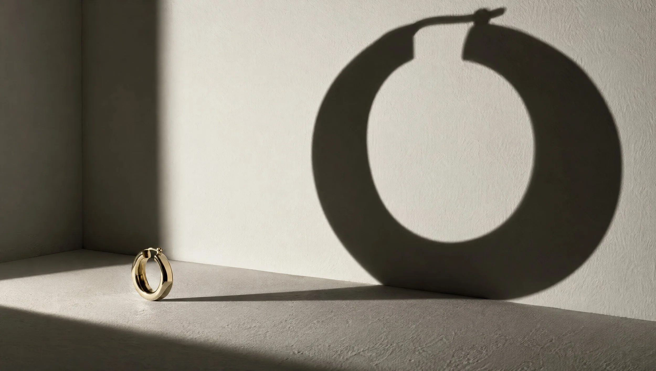 A gold hoop earring casting a large shadow on a pale wall.