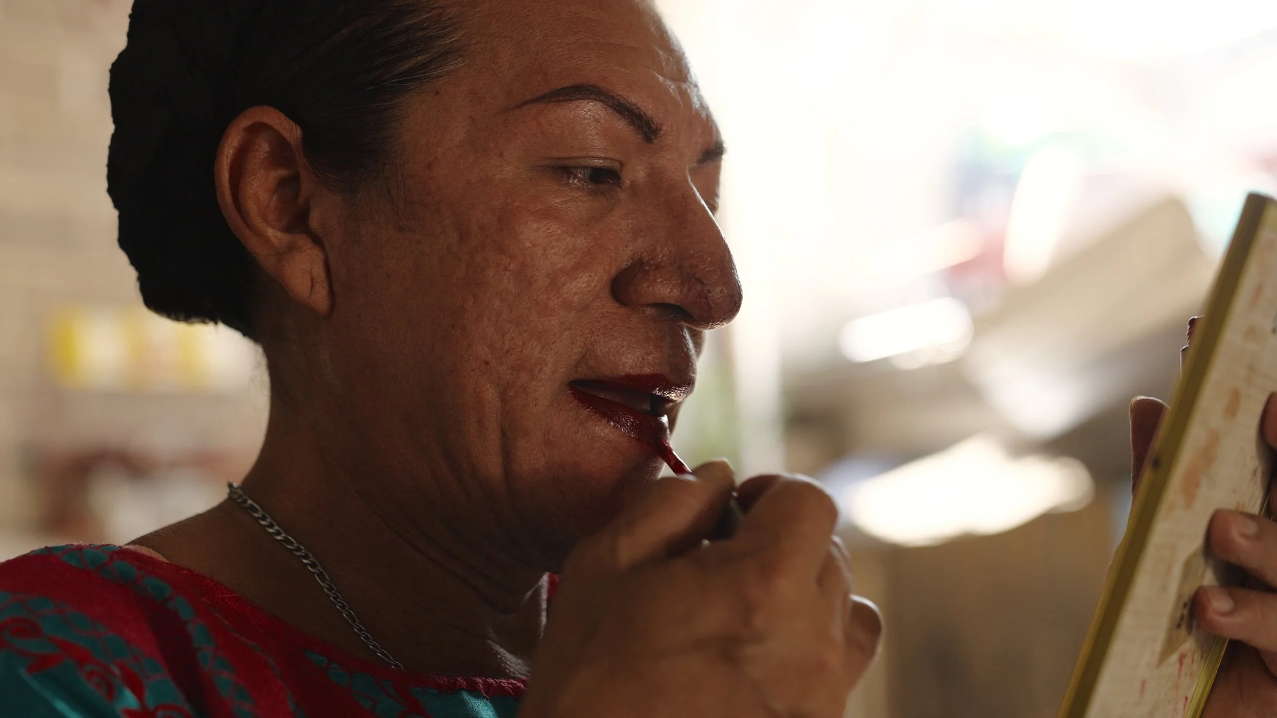 Una donna che si trucca le labbra con un rossetto rosso mentre si guarda allo specchio. Messico Muxe