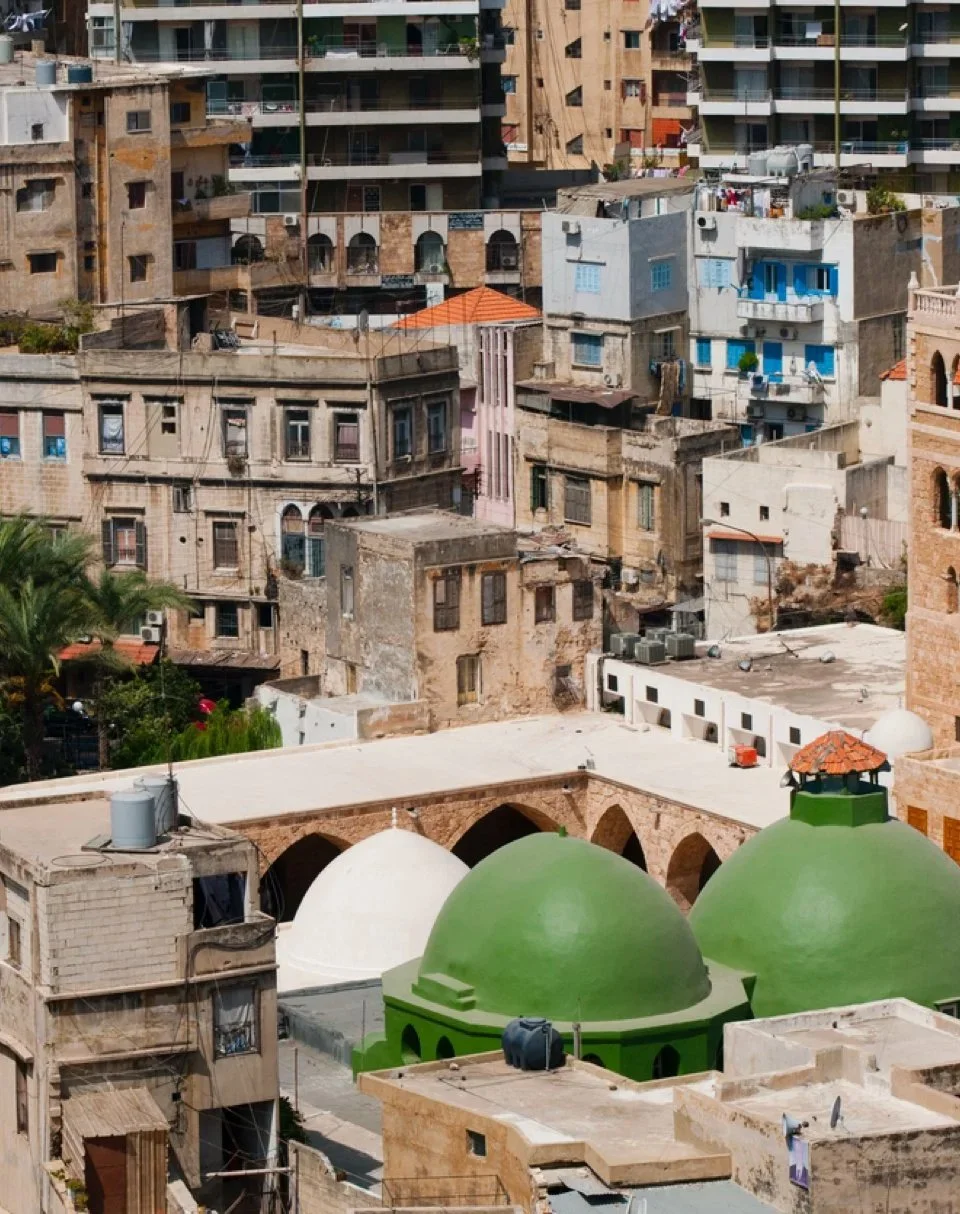 A densely packed urban area with various buildings. In the foreground, there are two green domes and one white dome, likely part of a mosque. The background features numerous old and new apartment buildings with different colors and architectural styles.