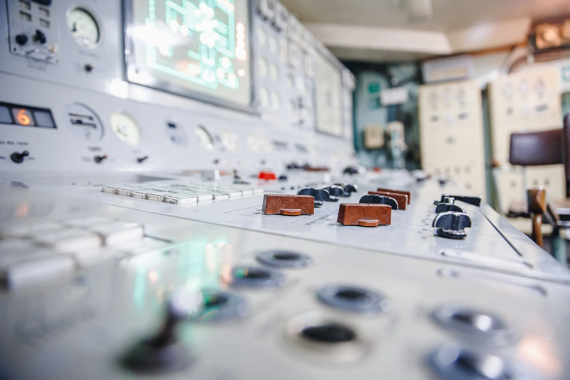 Close-up of an aviation control panel with switches and gauges, featuring a blurred background of additional equipment and lockers in a room.