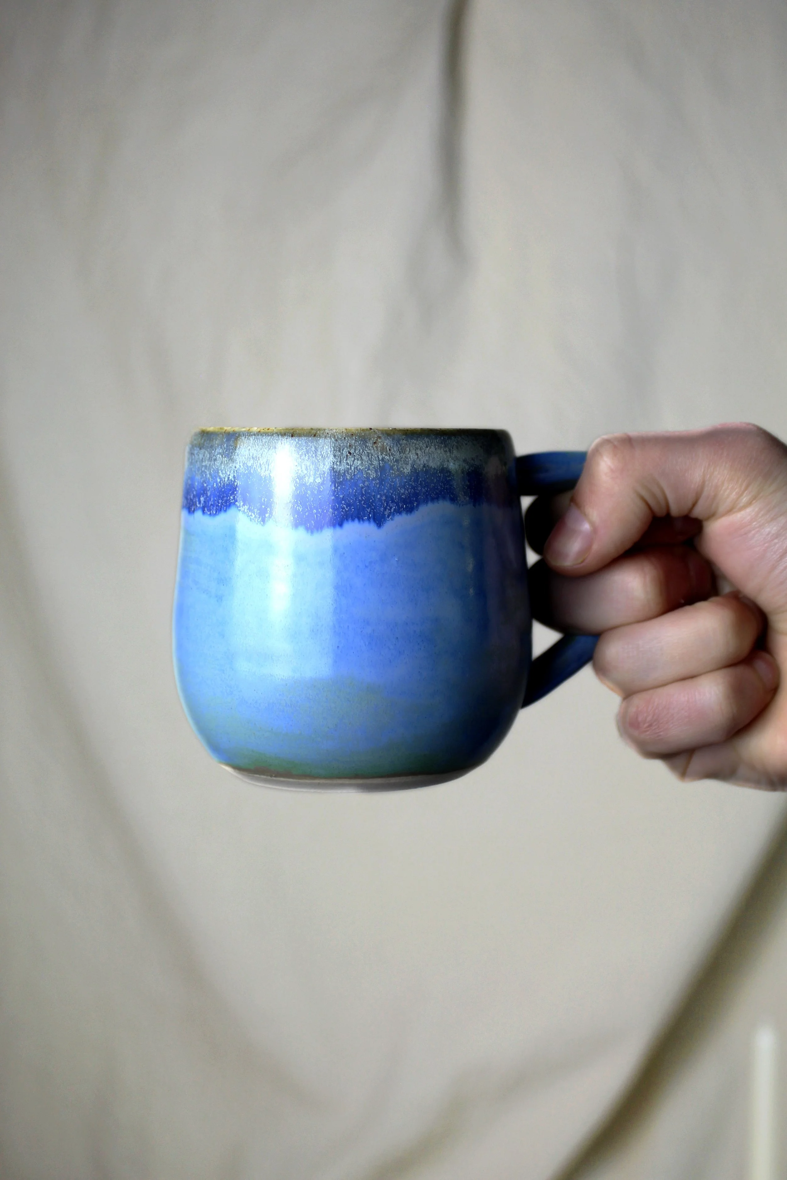 A hand holding a blue ceramic mug with a gold rim against a plain background.