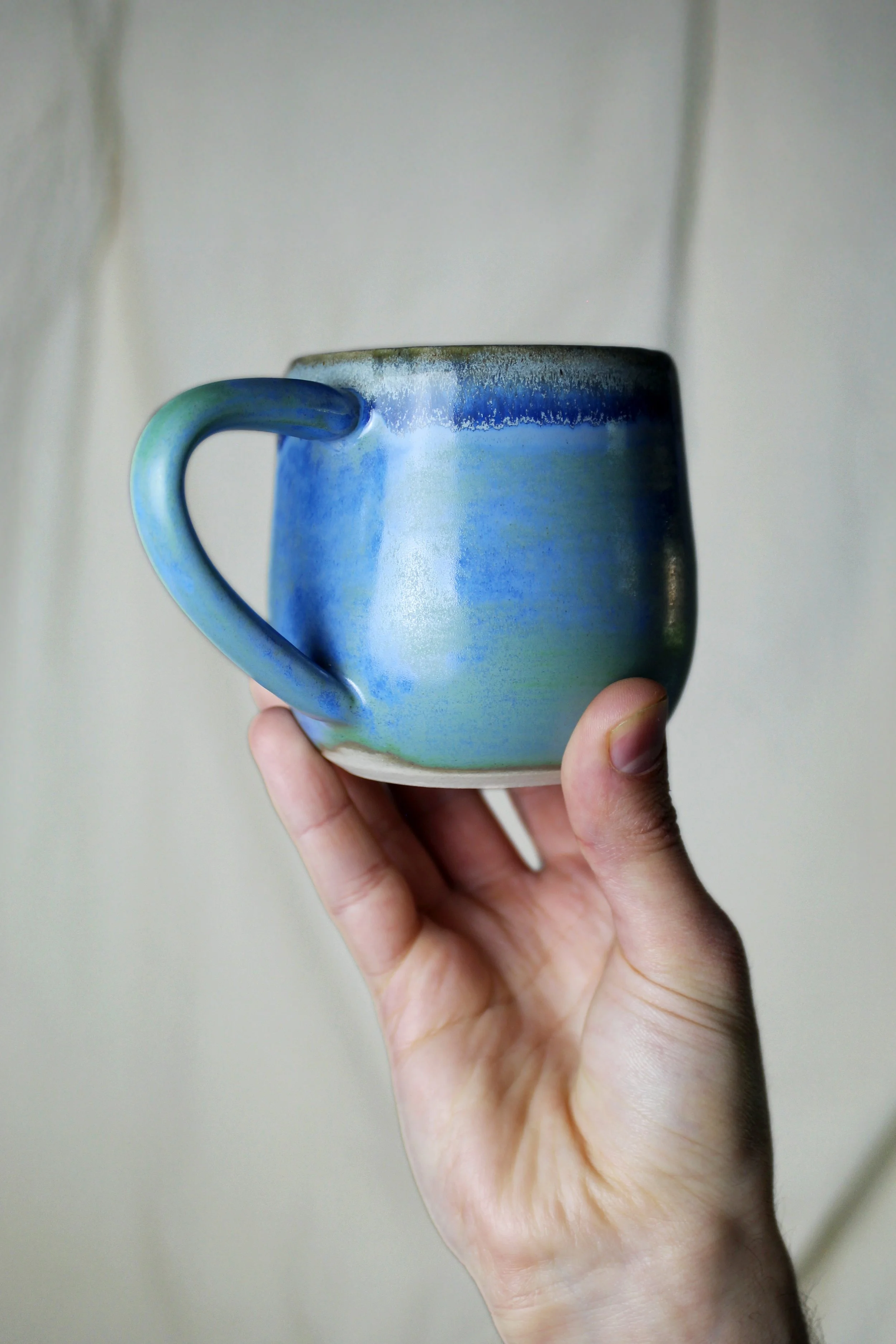 A hand holding a ceramic mug with a blue-green gradient glaze