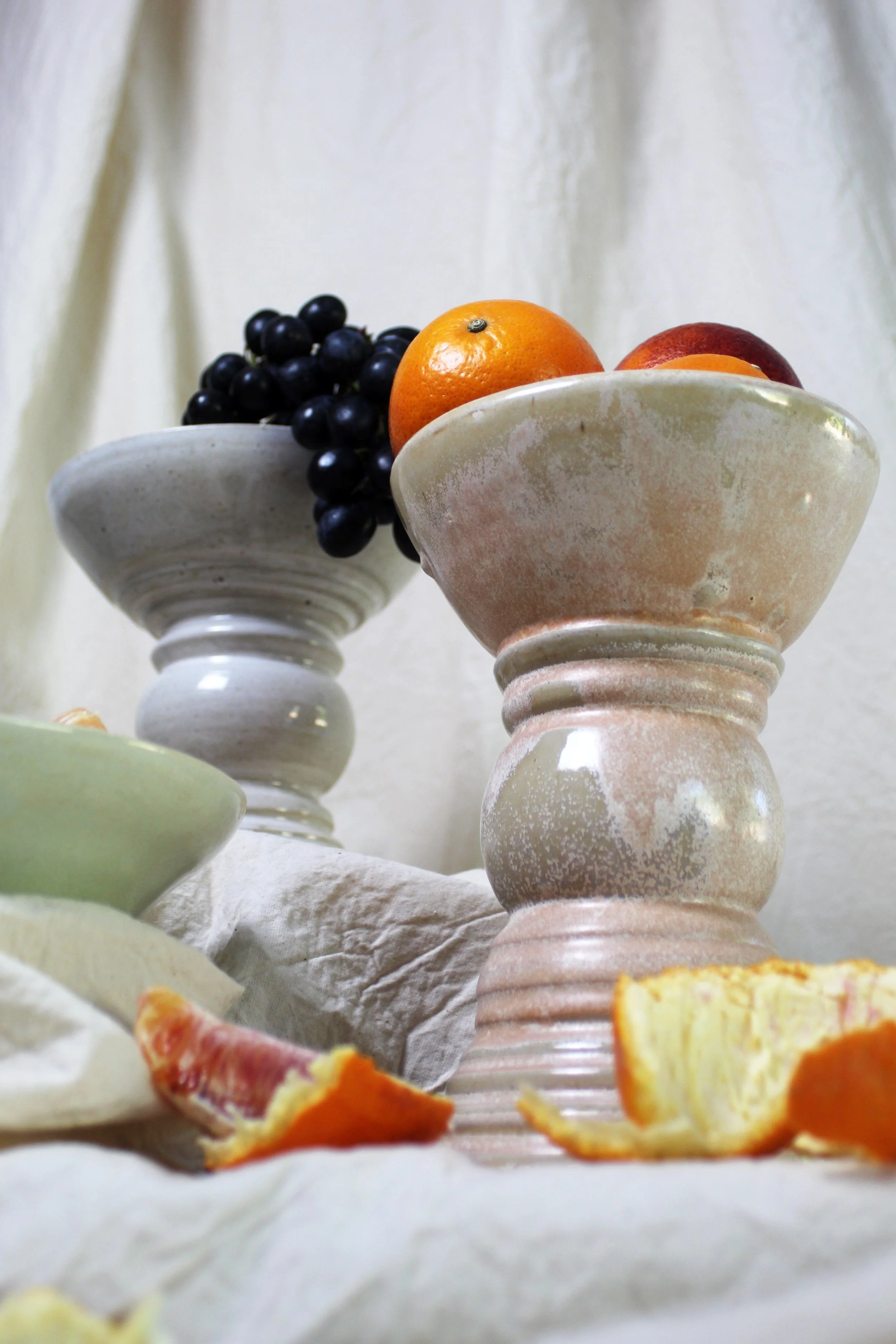 Close-up of decorative ceramic bowls with grapes and oranges on a fabric surface.