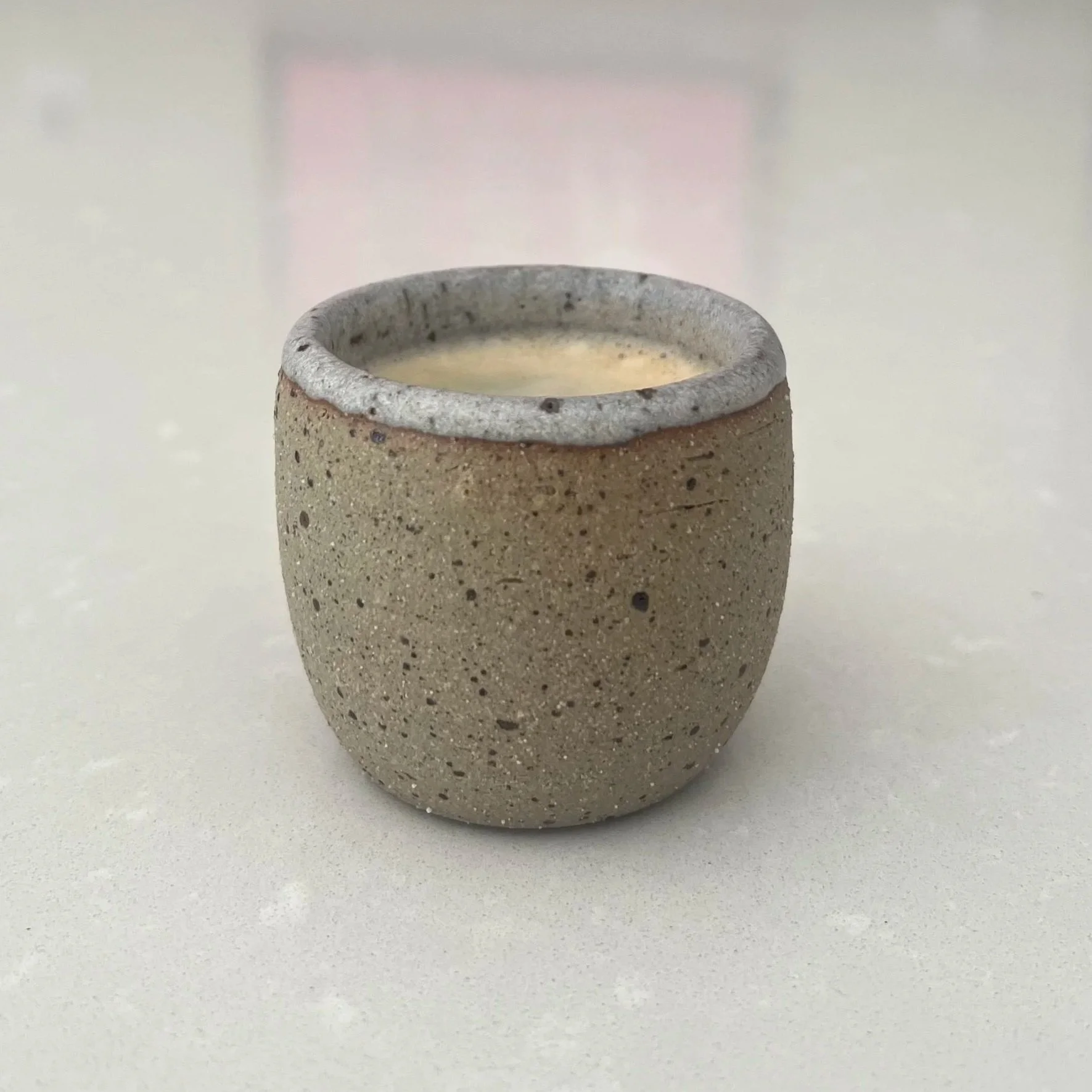 A speckled lava-flecked exterior in warm sandy yellow, finished with a cool beige granite rim and interior. Filled with hot espresso on a white kitchen island surface.