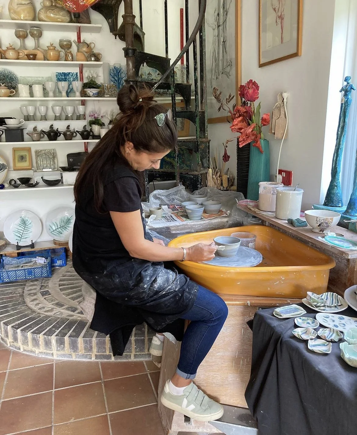 A ceramicist working at a pottery wheel in her studio, shaping a small clay vessel.