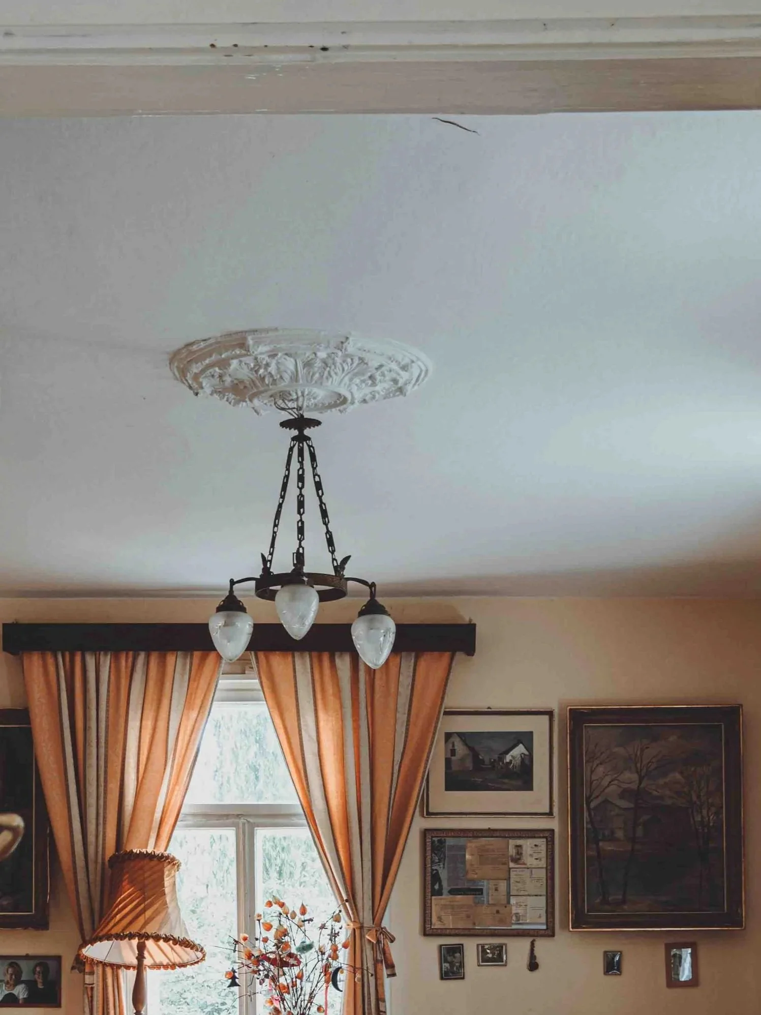 White ceiling with brass chandelier hanging in a room with orange striped curtains and picture frames on wall