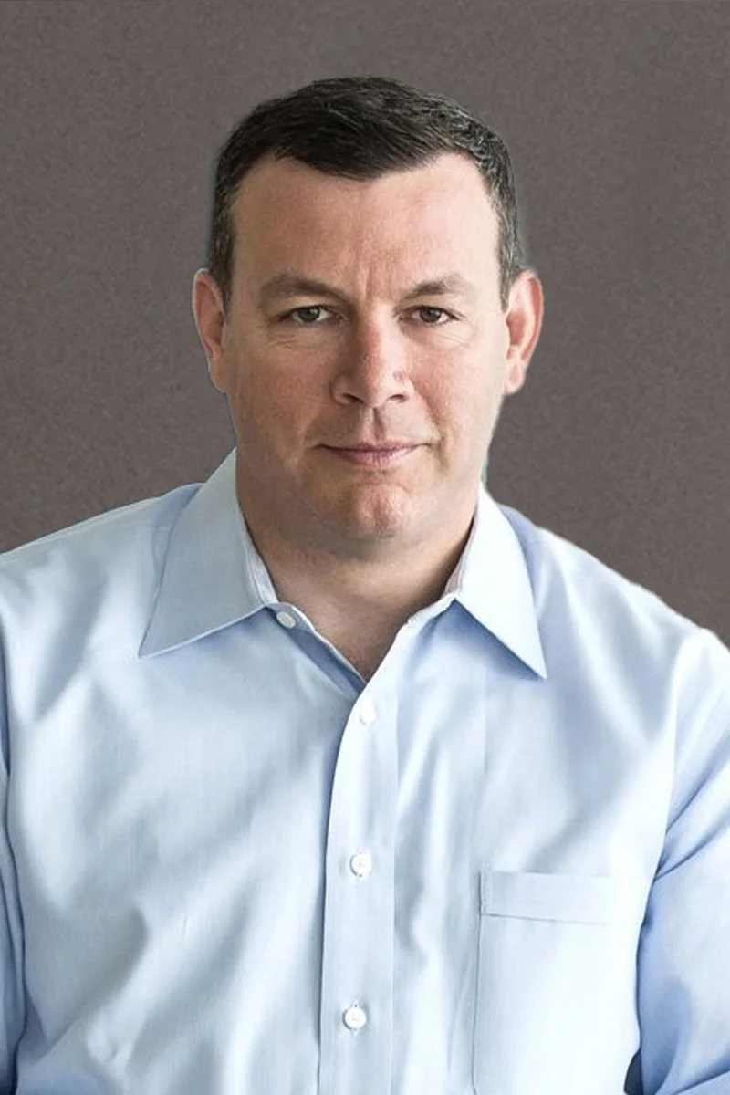 Headshot of a man in a light blue button-up shirt against a plain background.