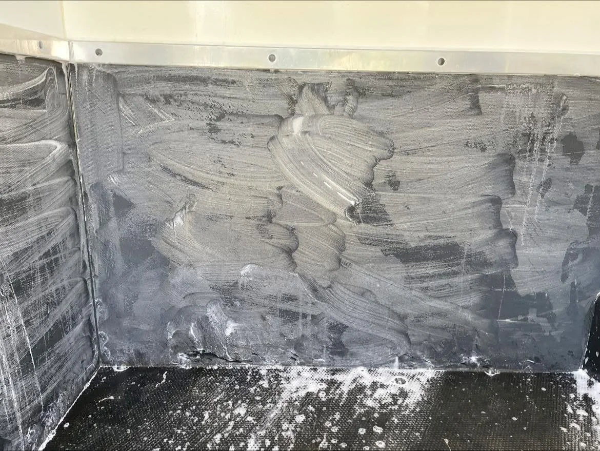 A stainless steel kitchen wall with smeared white cleaning foam or soap, and some scattered foamy residue on the black textured floor.