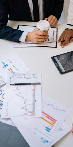 People in business attire discussing and reviewing charts and graphs with a cup of coffee on a work desk.