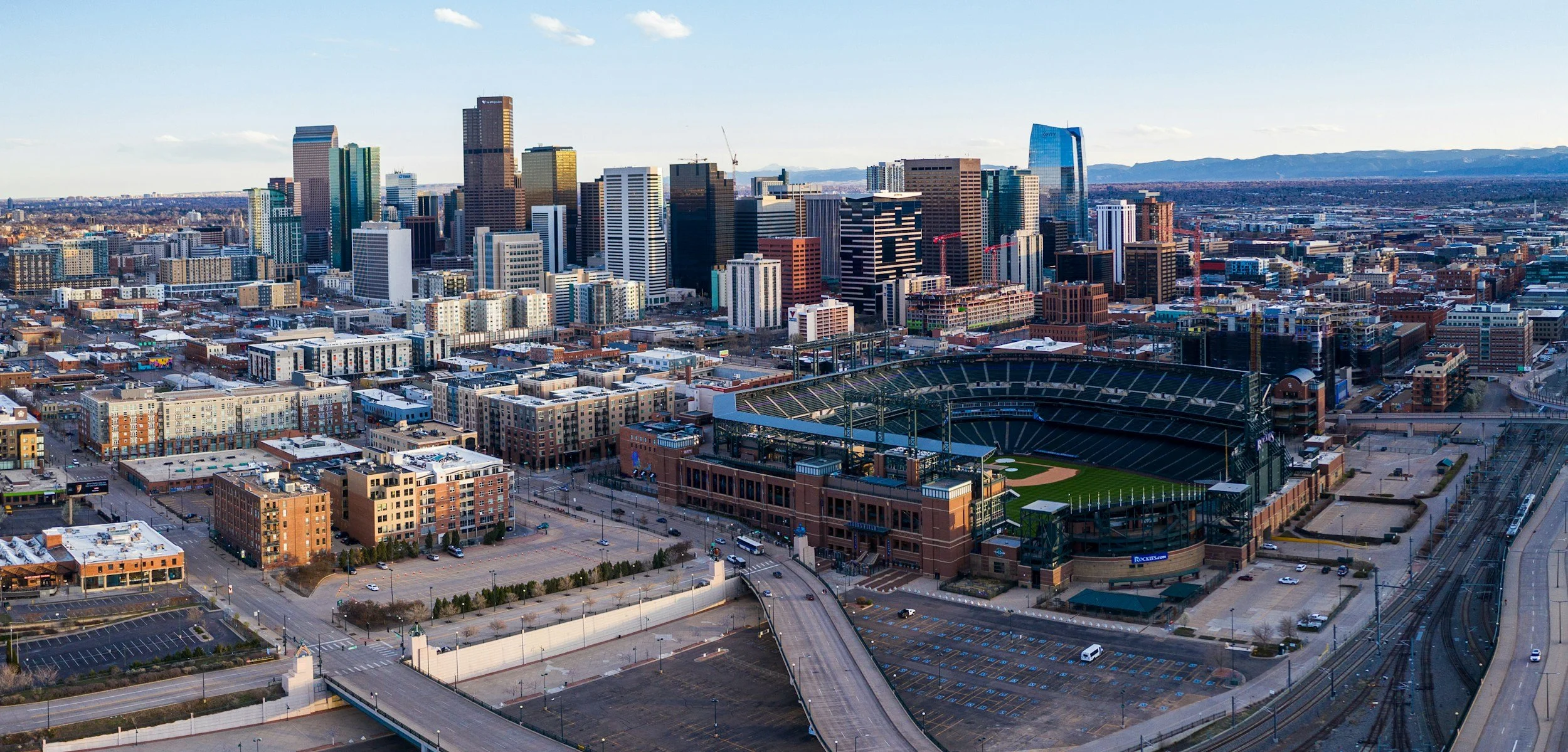 Aerial view of downtown Los Angeles with skyscrapers, sports stadium, and surrounding cityscape under a clear sky.