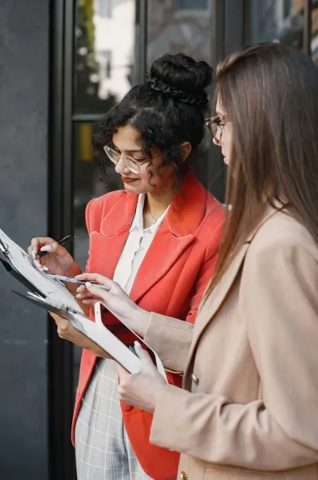 Two executive women talking and looking at something in an open folder together.