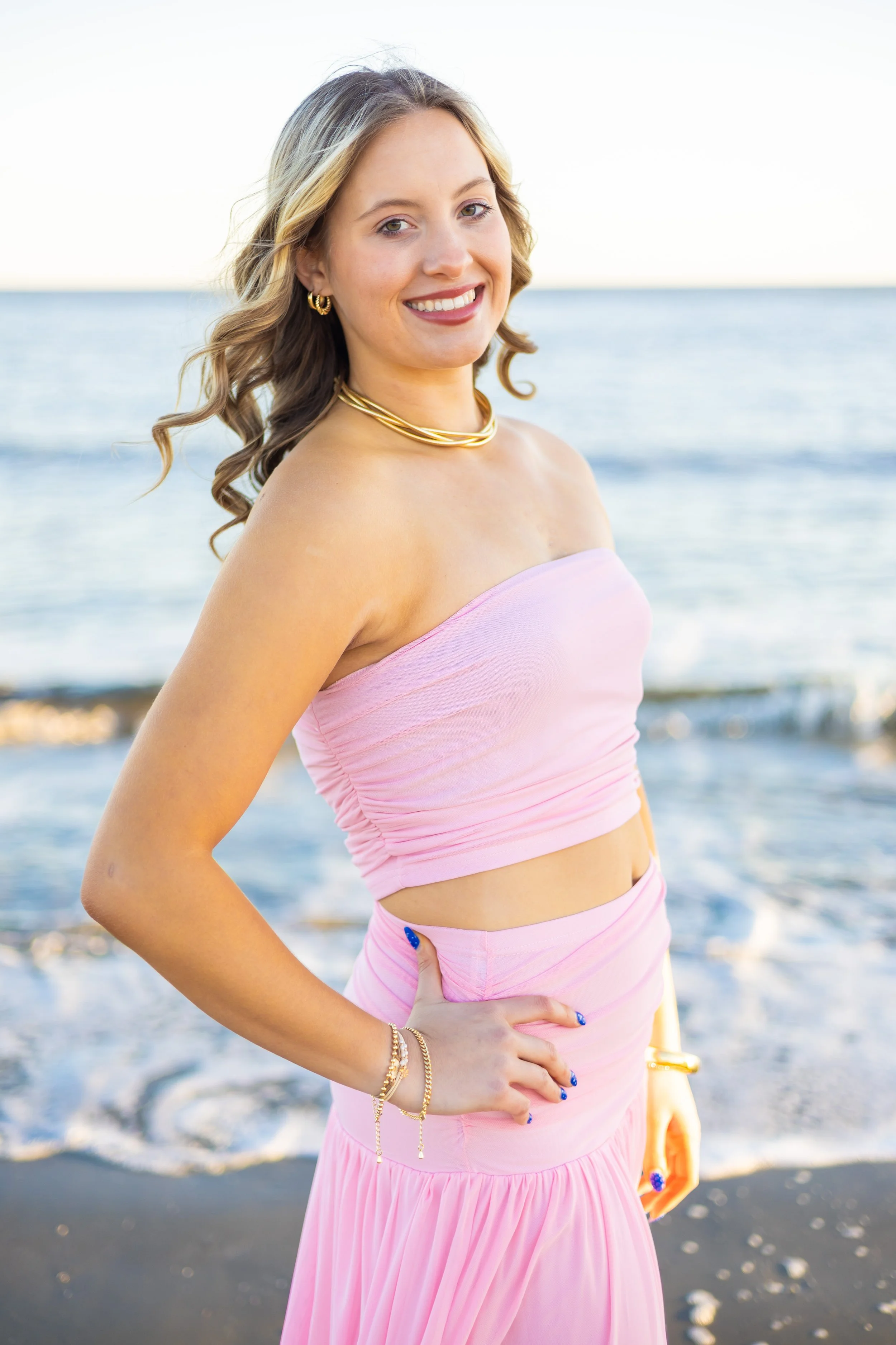 senior girl on beach in pink dress with gold jewelry