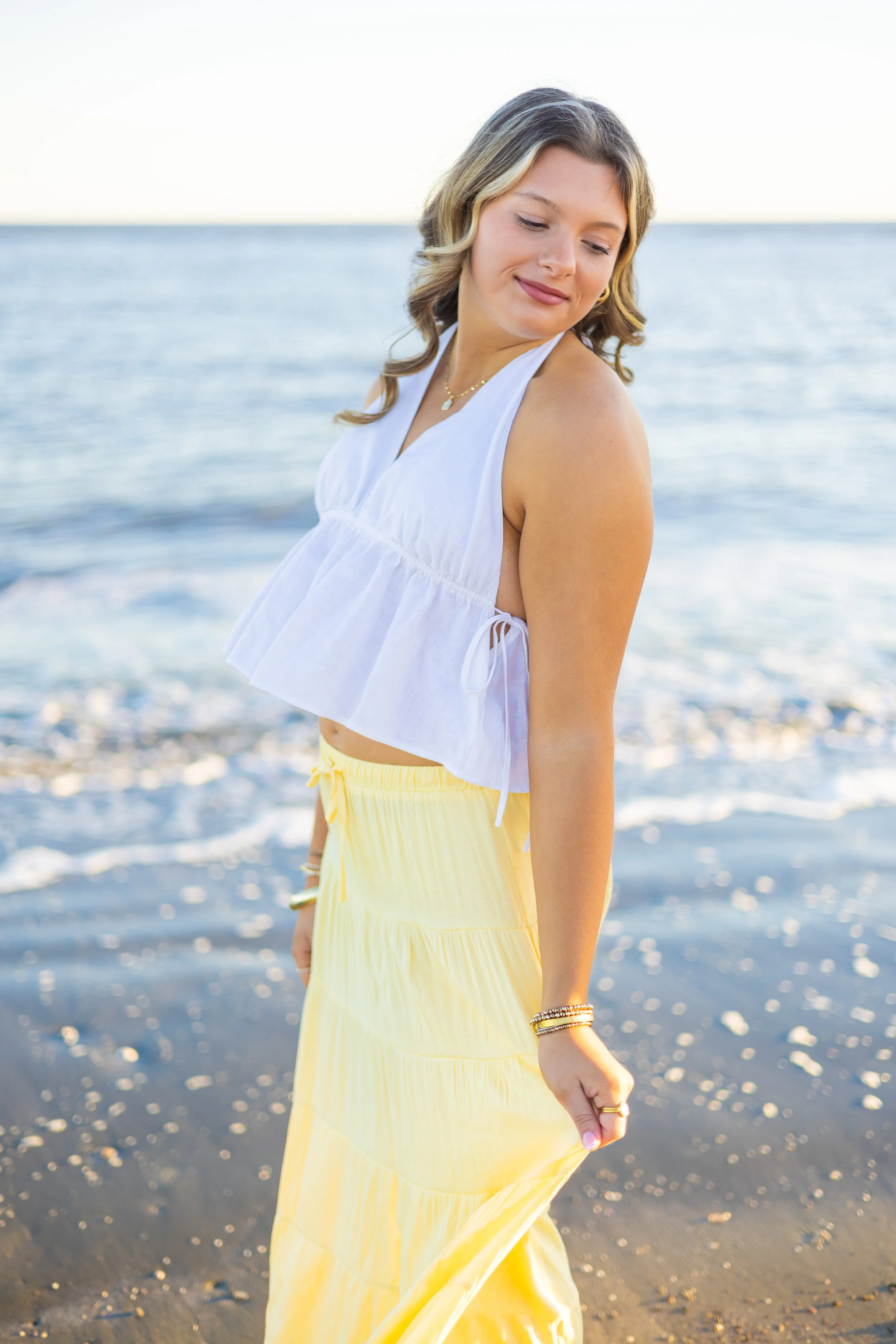 blonde senior girl on the beach in white top and yellow skirt