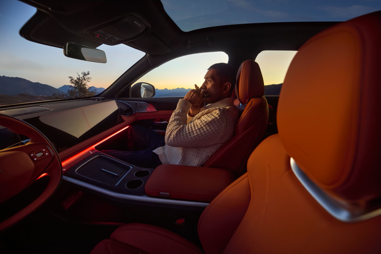 Un homme assis dans une voiture au coucher du soleil dans un paysage de montagnes.
