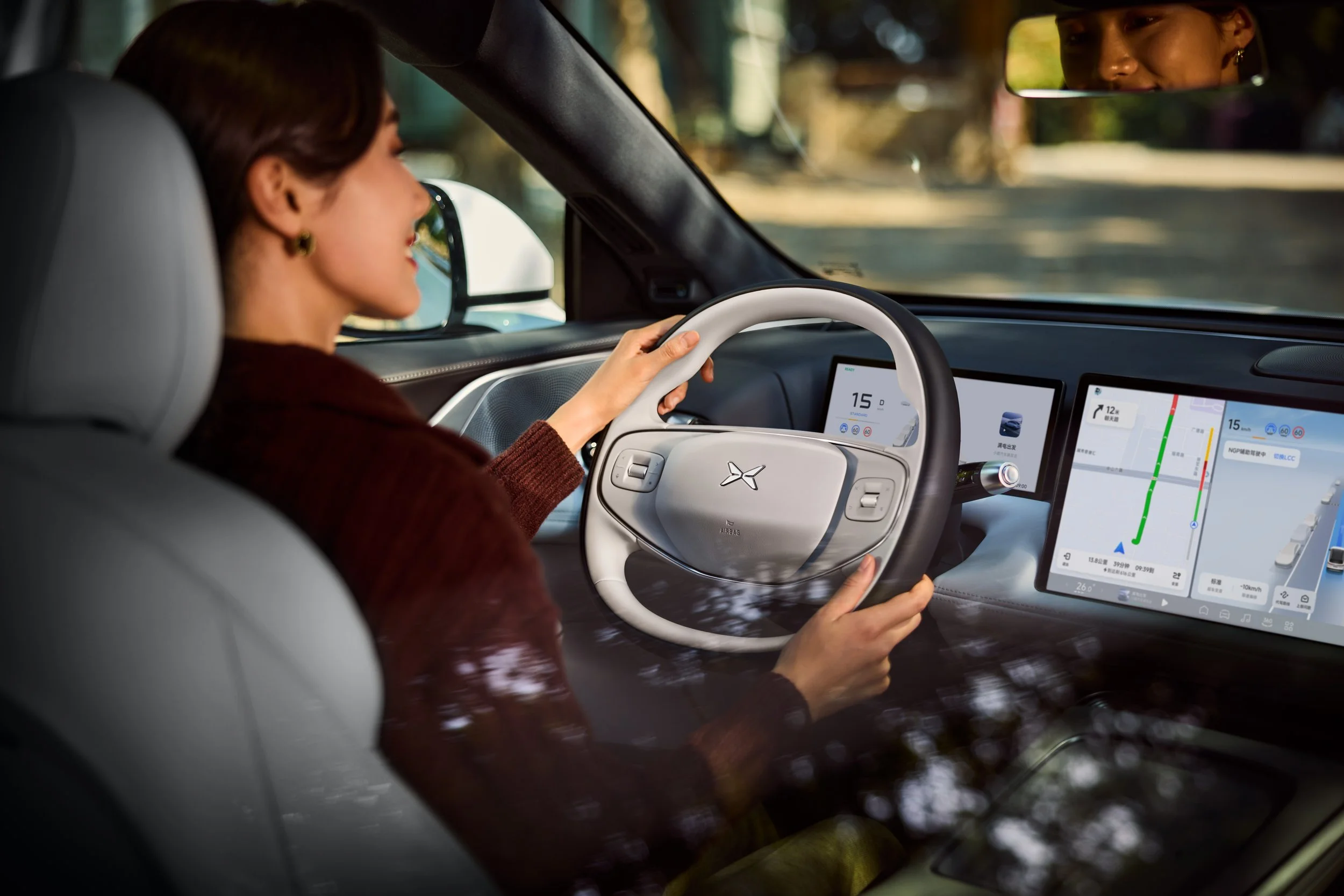 Une femme conduit une voiture avec un tableau de bord numérique et un grand écran tactile affichant des données de navigation et de performance.