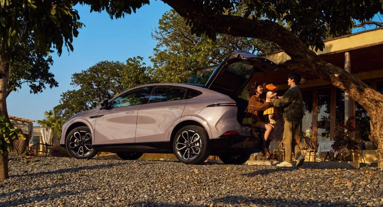 Famille avec un enfant à côté d'une voiture électrique garée devant une maison, dans un environnement naturel.