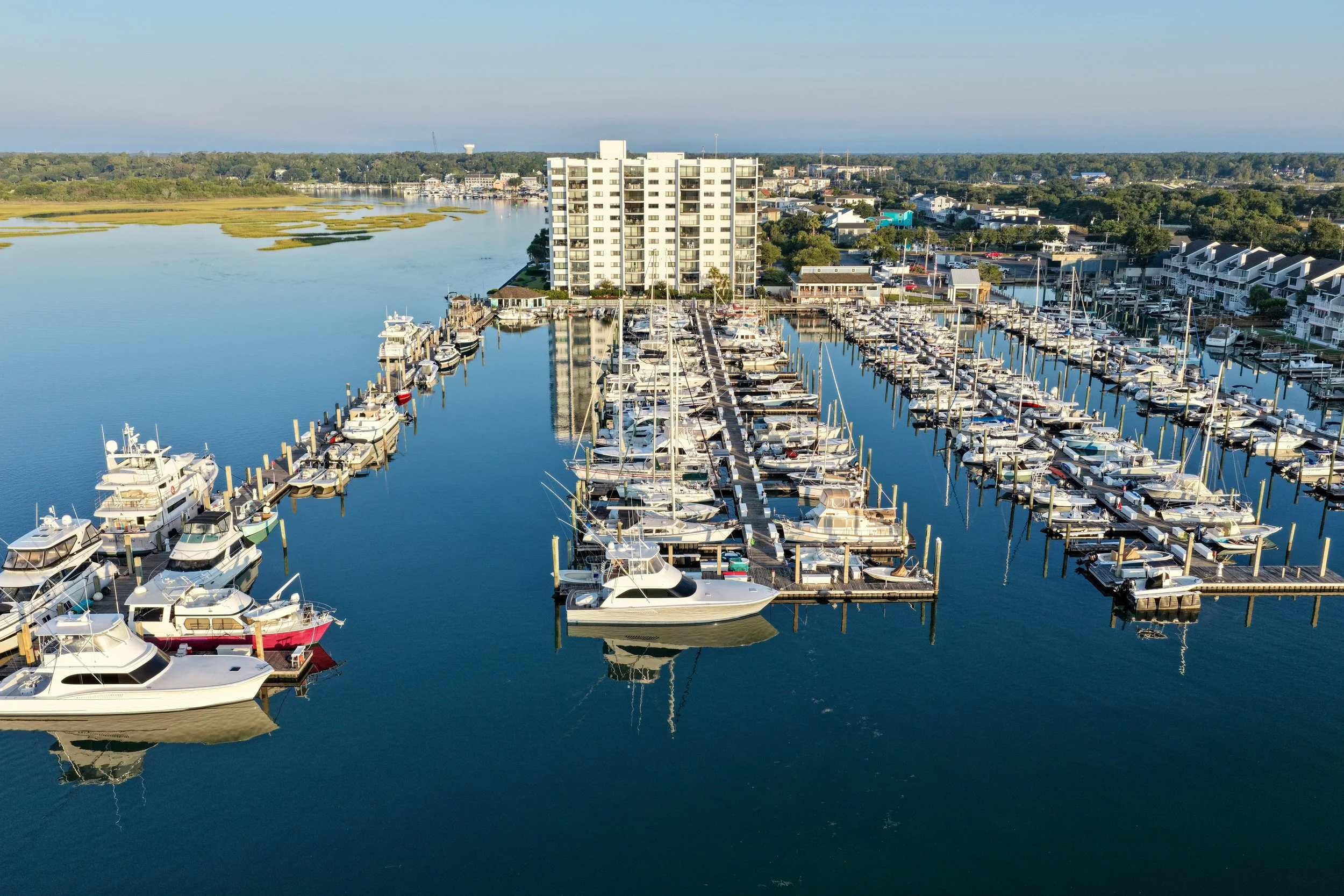 A marina with many boats docked in water, with a white multi-story building and a town in the background.