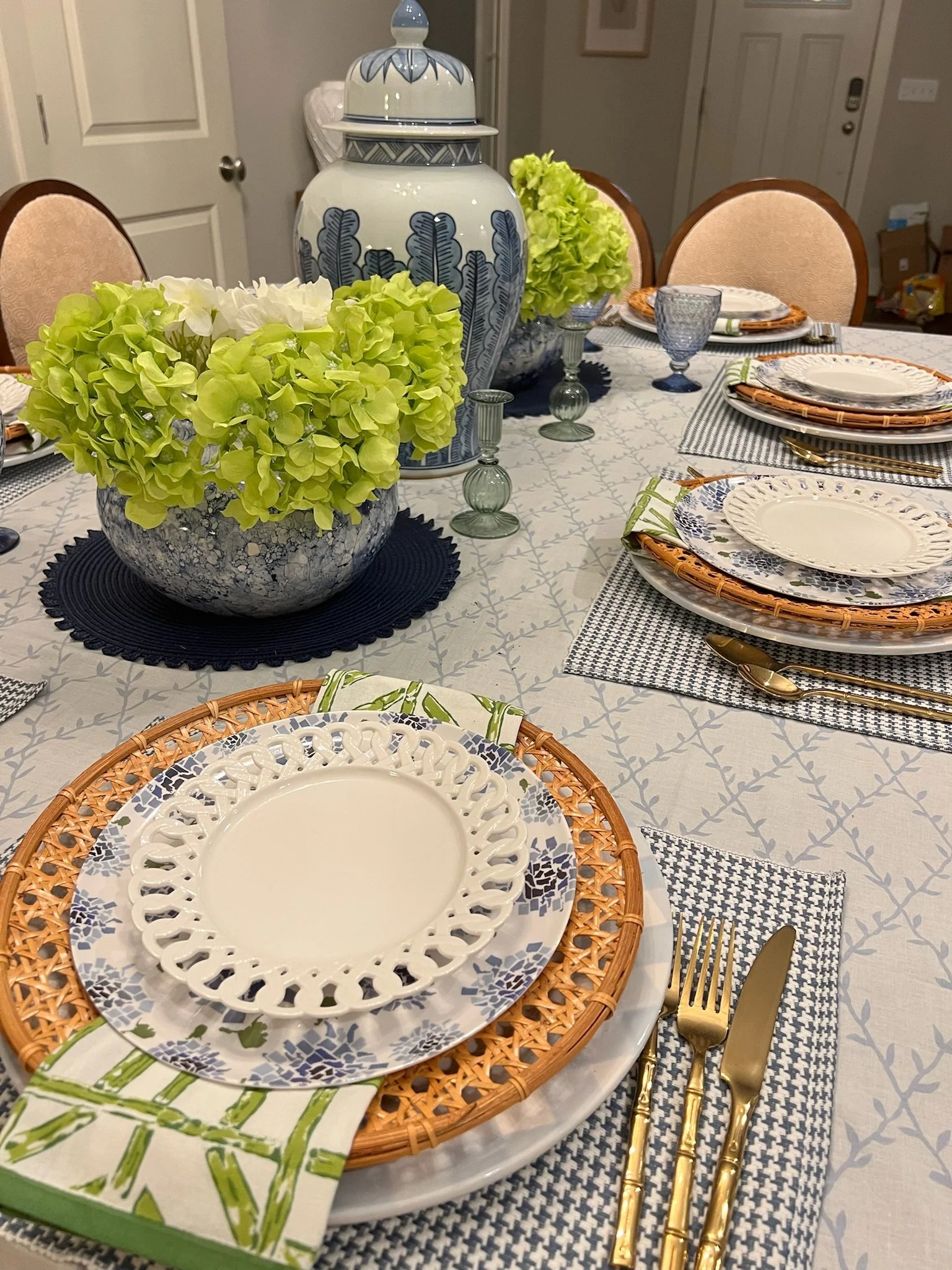 A dining table set with plates, gold utensils, wine glasses, and floral centerpieces, featuring a white tablecloth with a subtle gray pattern.