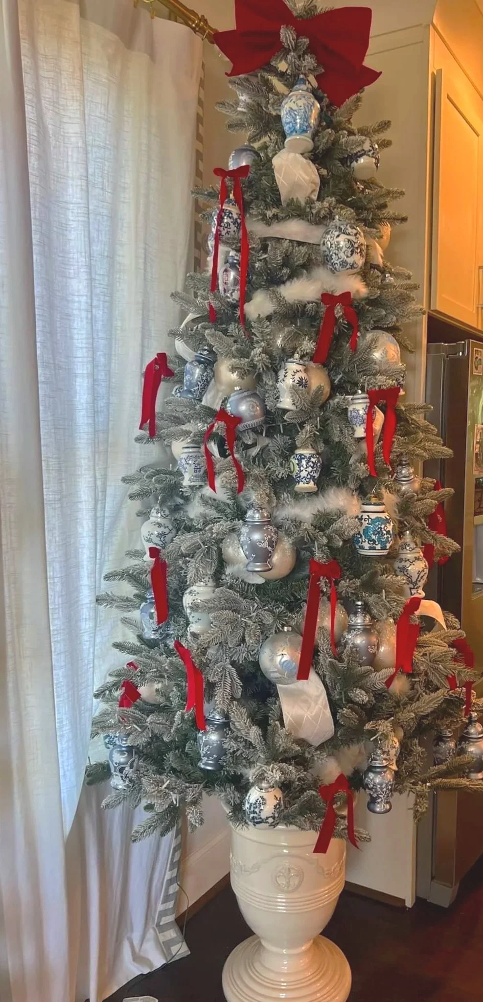 Chic Christmas tree with chinoiserie ornaments, red ribbons, white faux fur, and a red bow on top in a white urn. Ralph Lauren aesthetic.