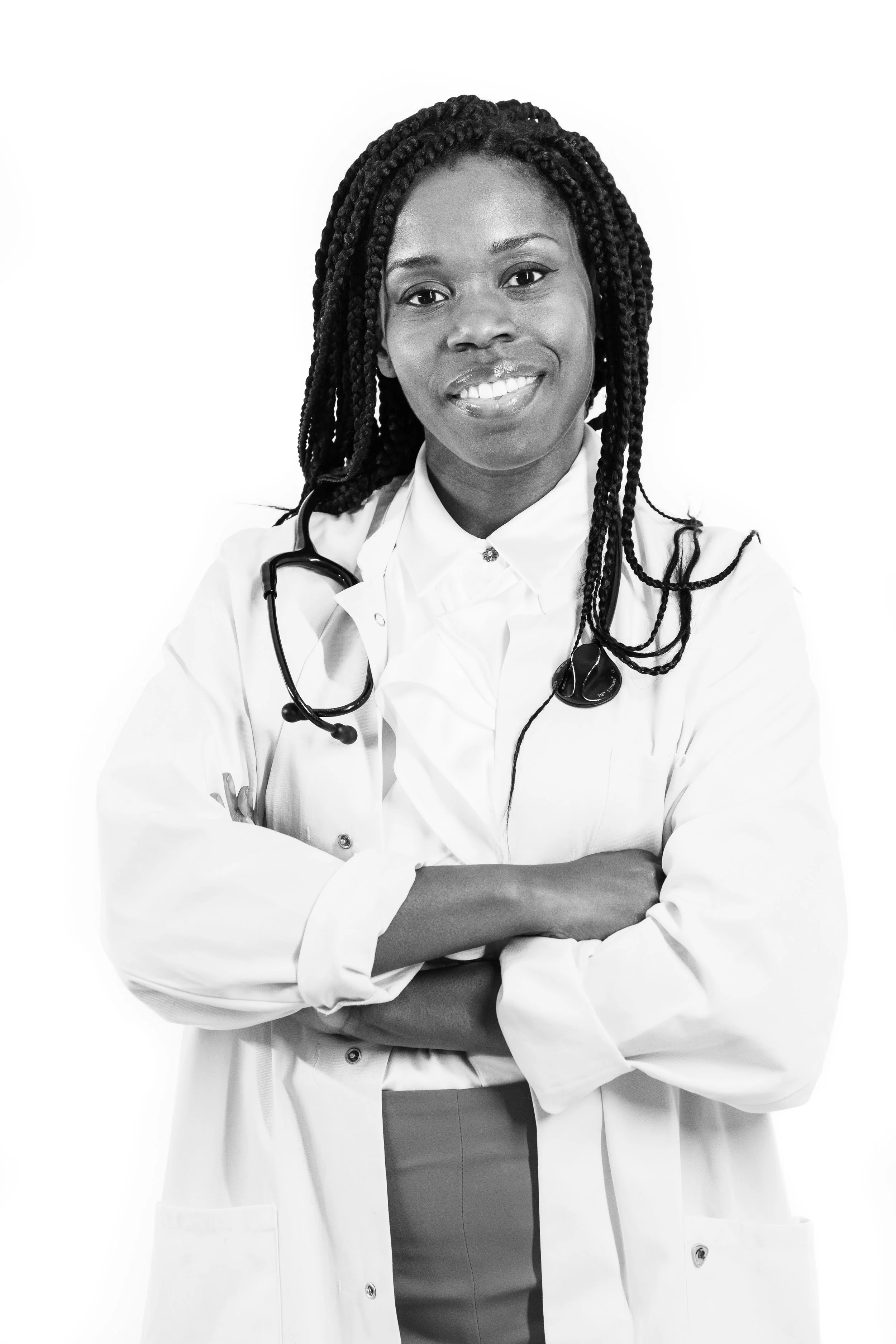Black and white photo of a female healthcare professional with braided hair, smiling, wearing a white coat and stethoscope, with arms crossed.
