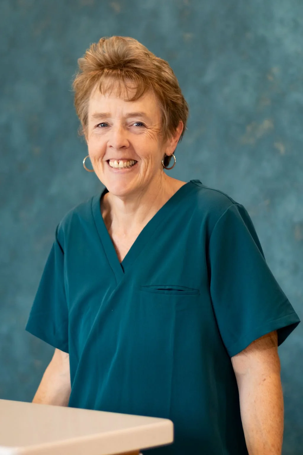 Smiling woman in teal scrubs standing against a blue background.
