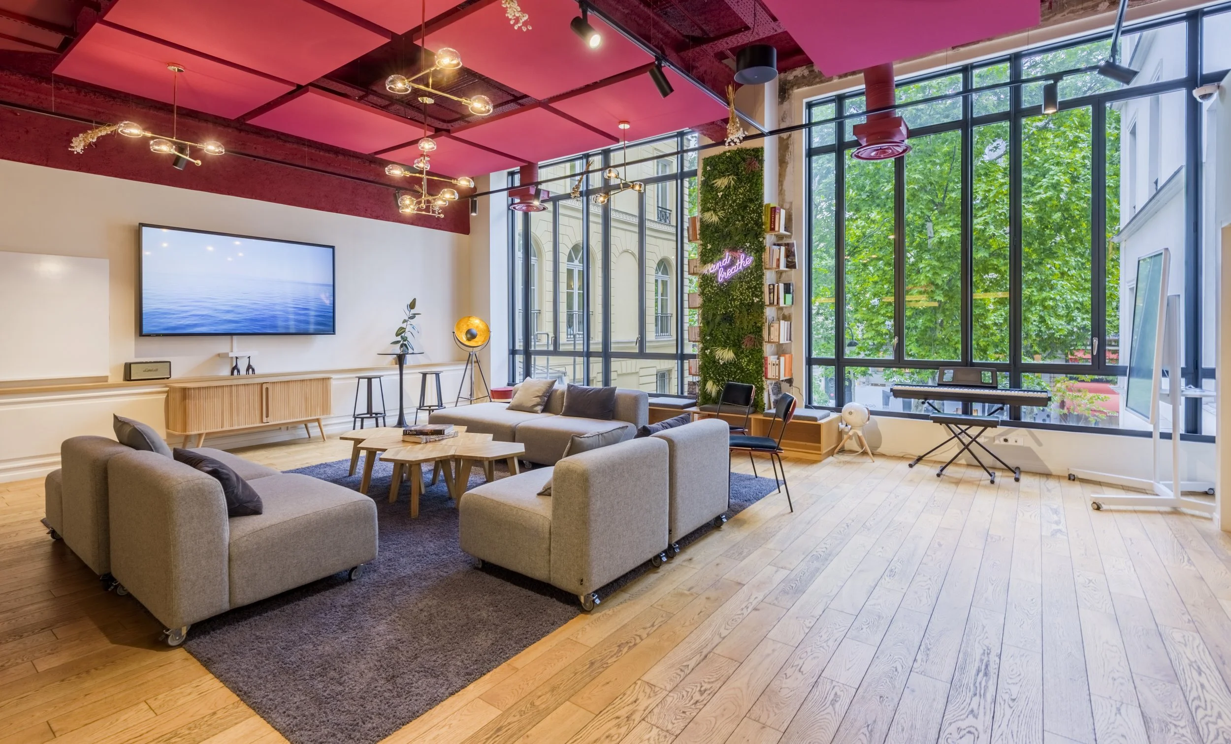 Salon moderne avec canapé, tapis, tables en bois, grande fenêtre, bibliothèque avec plantes et accessoires lumineux