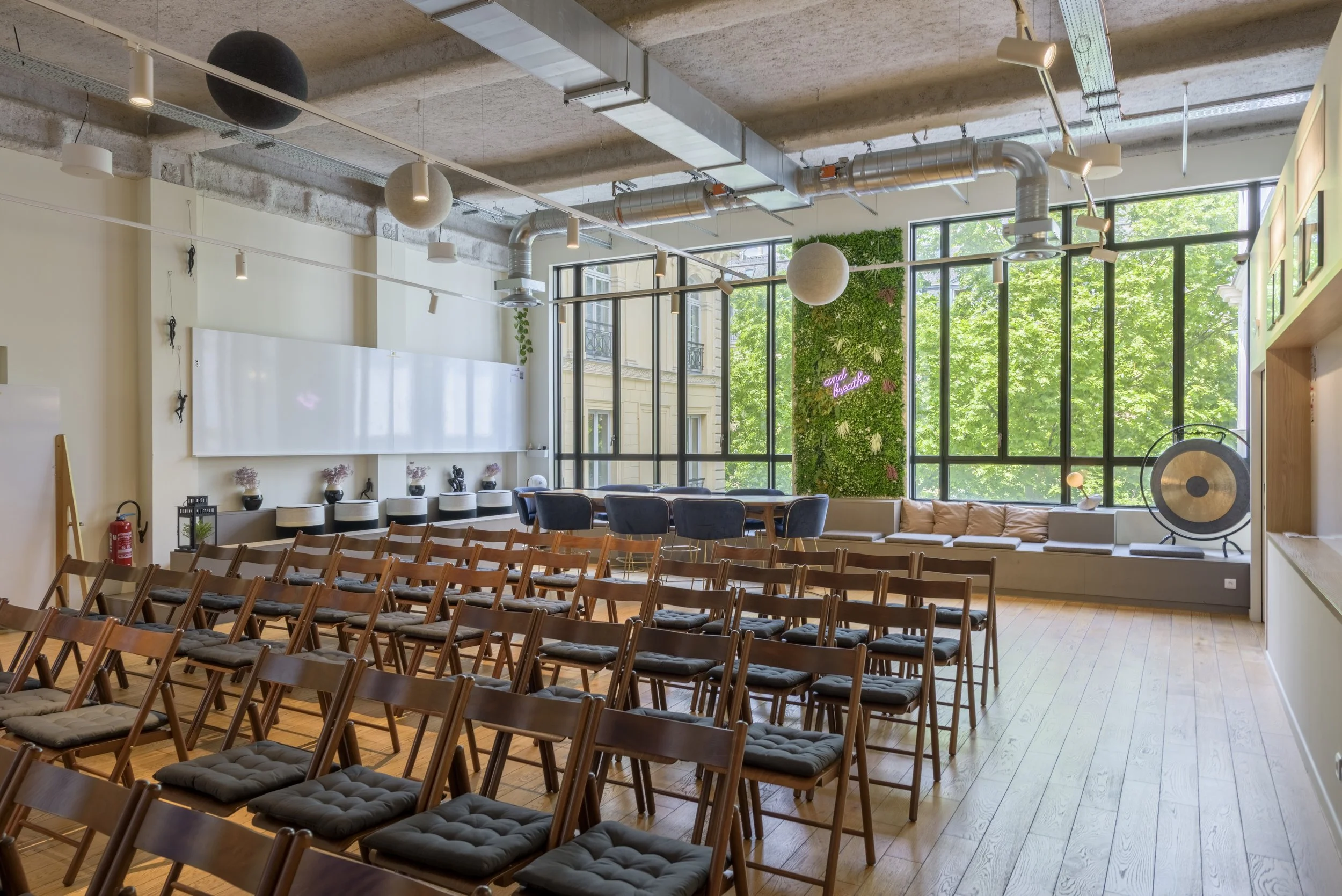 Salle de réunion ou conférence avec chaises en bois, grande fenêtre avec vue sur des arbres, mur végétal, décor moderne et lumineux.