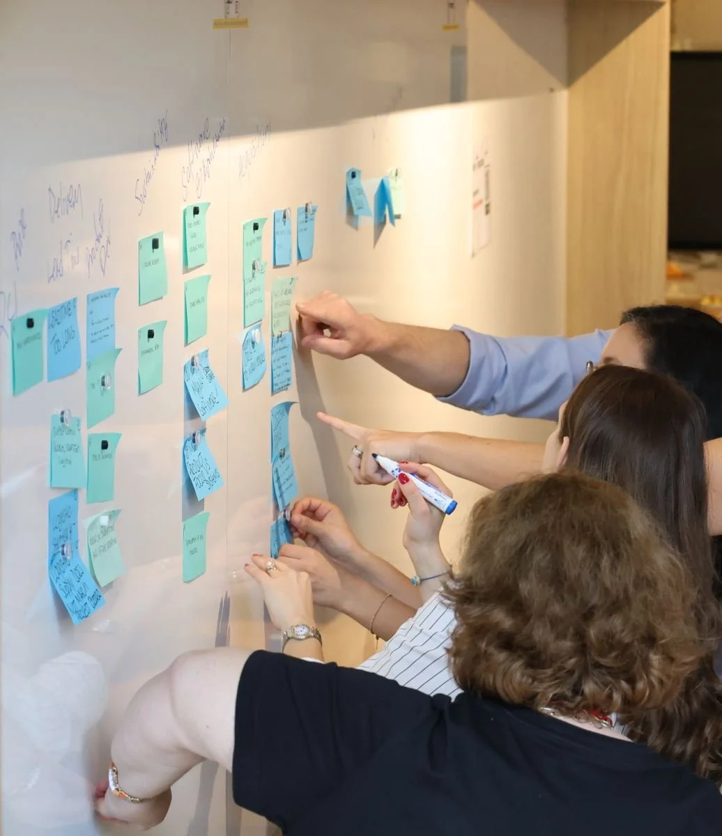 Groupe de personnes discutant et pinçant des notes en post-it bleues sur un tableau blanc lors d'une réunion ou séance de brainstorming.